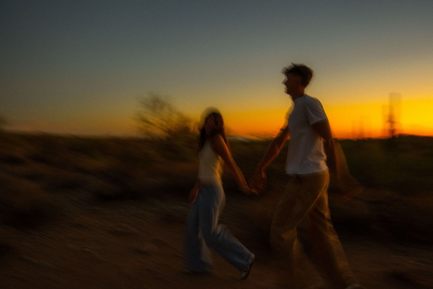 Silhouetted figures walk along a desert path against a vibrant orange sunset sky.