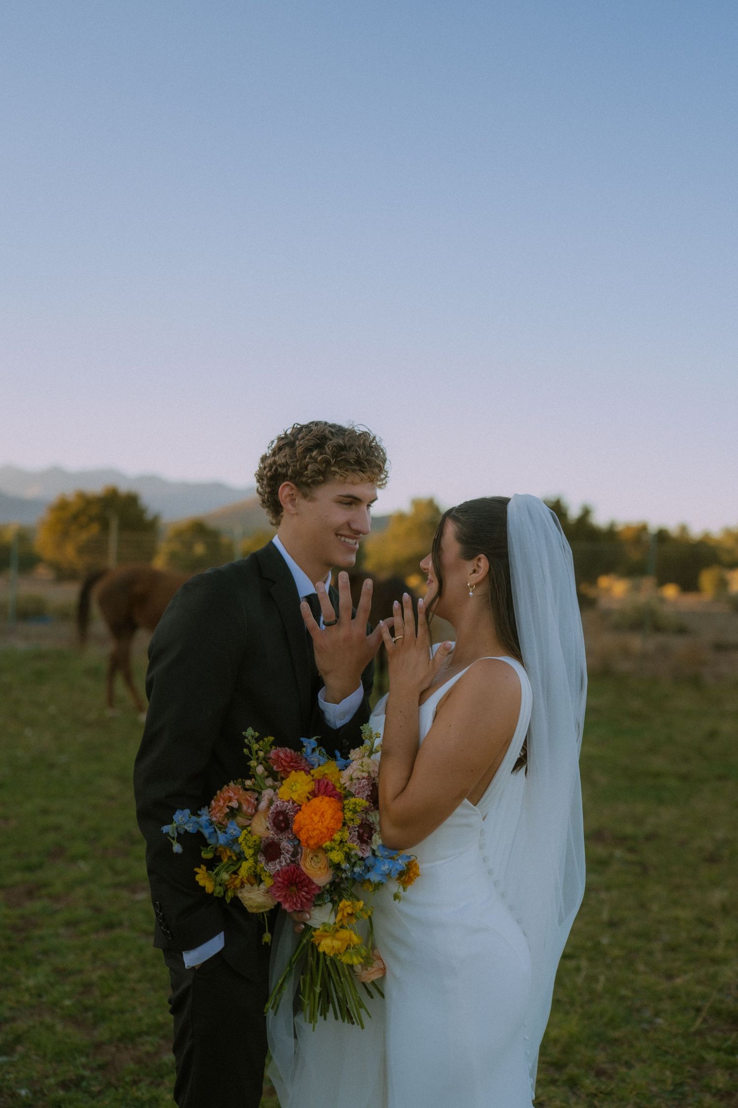Romantic wedding couple shares intimate moments at sunset in a field with vibrant wildflower bouquet.