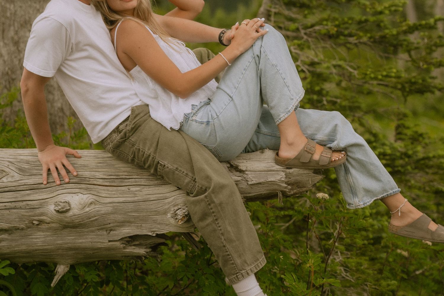 Two people sitting close together on a rustic wooden bench surrounded by lush greenery.