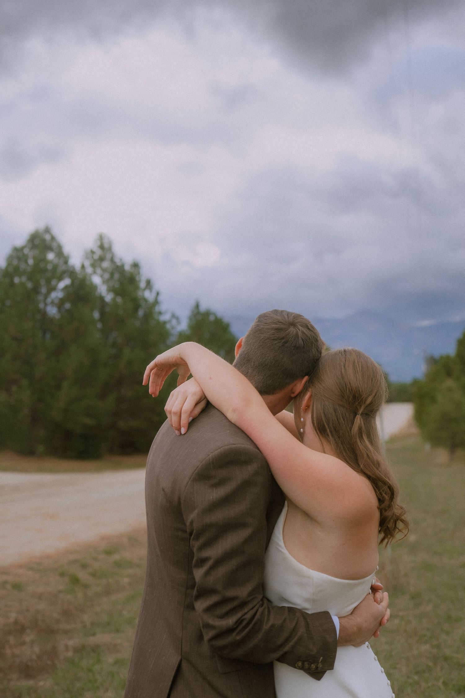 A couple embraces intimately during their outdoor wedding photoshoot with evergreen trees in the background.