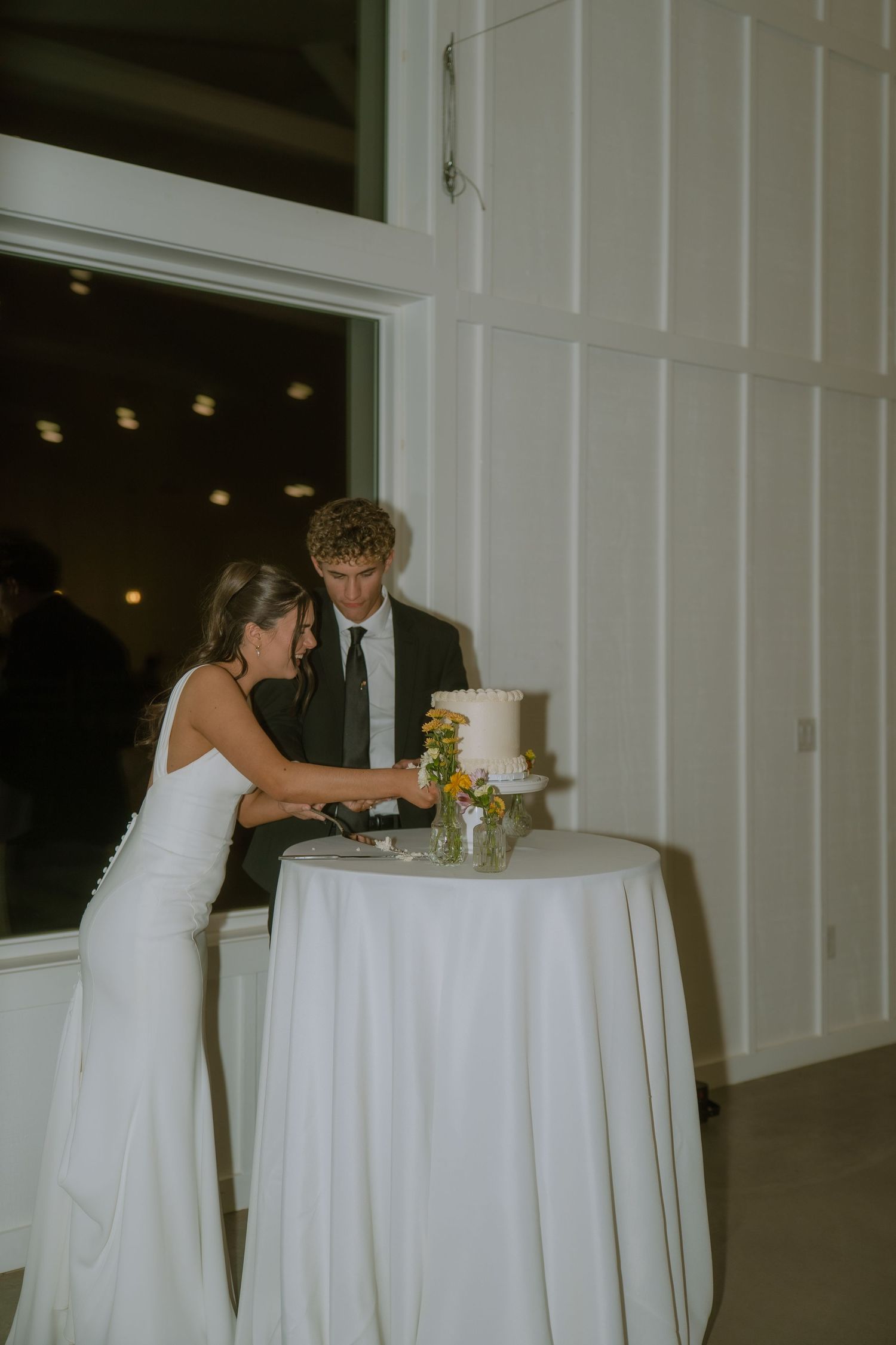 Wedding cake cutting scene at an elegant white-themed indoor reception.