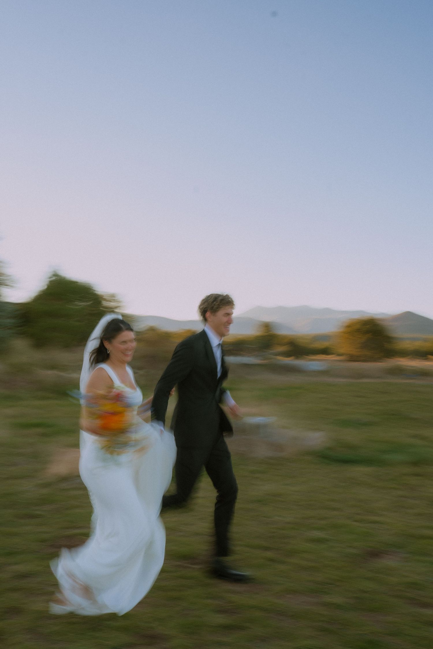 Motion-blurred photo of couple walking across field with mountains in background.