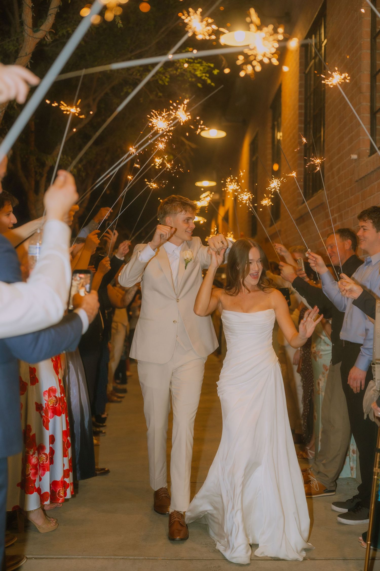 Newlyweds walk through a sparkler exit tunnel at night while guests hold lit sparklers creating a magical atmosphere.
