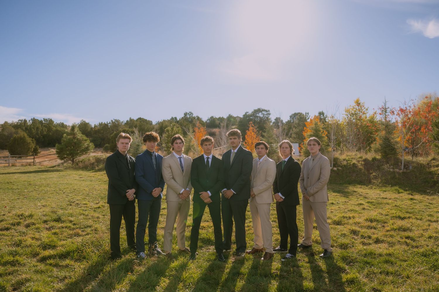 Groomsmen lined up for a formal photo in an outdoor setting with autumn scenery.
