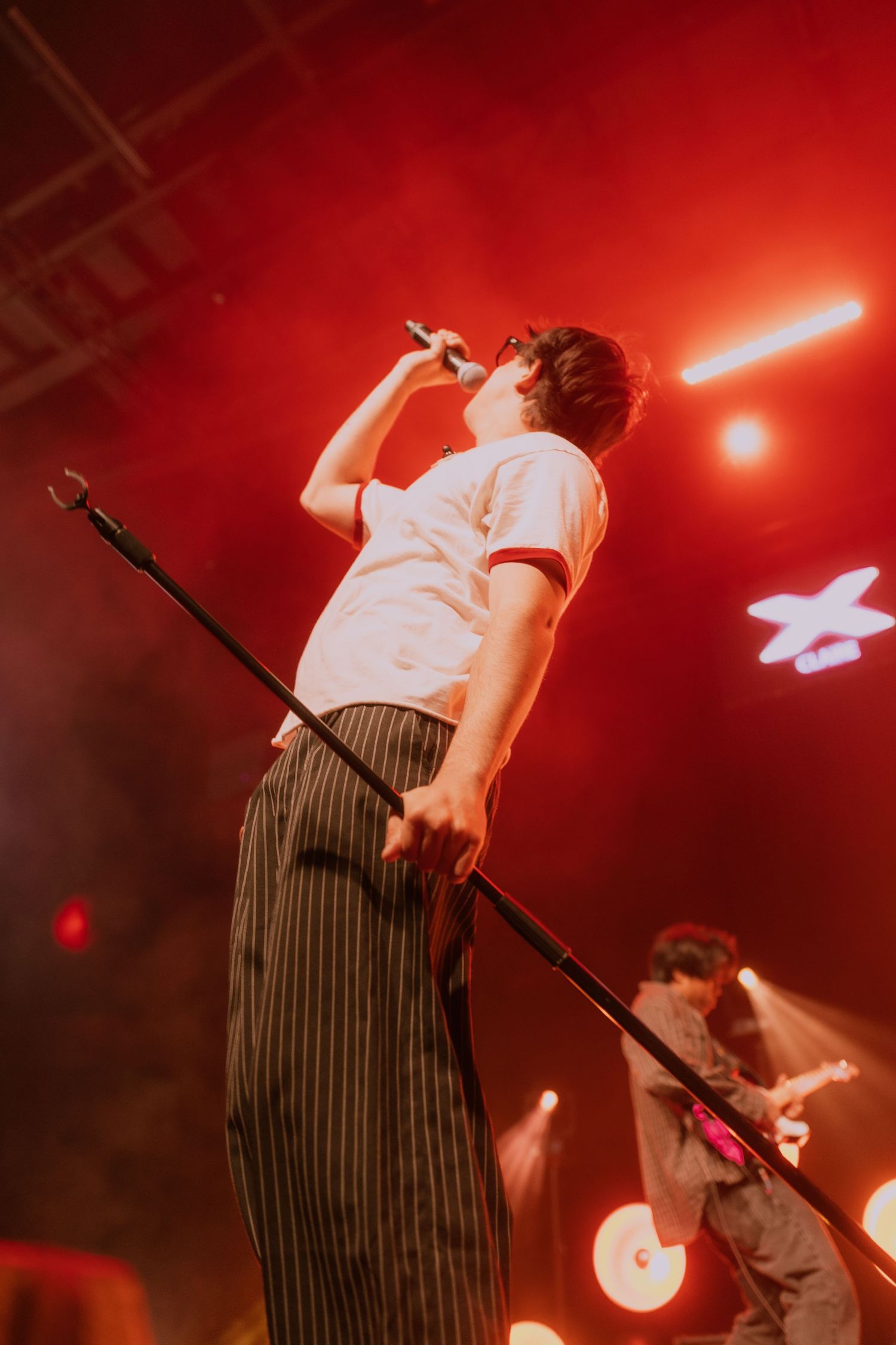 Concert performer in striped pants singing on stage with dramatic red lighting and spotlights during live performance.