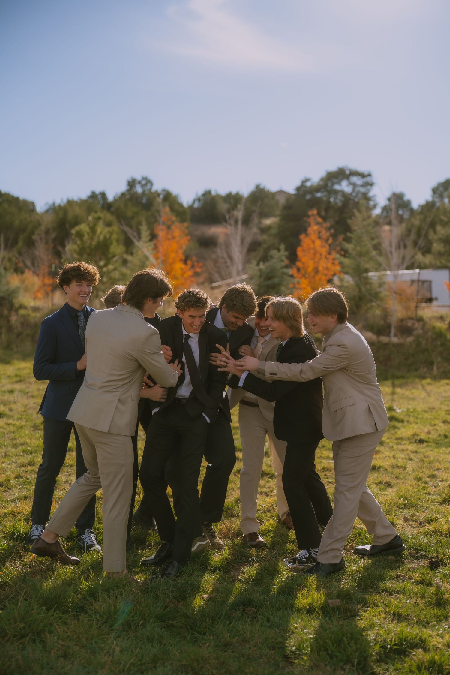 Groomsmen in suits huddle together on grass during sunset for a fun group photo.