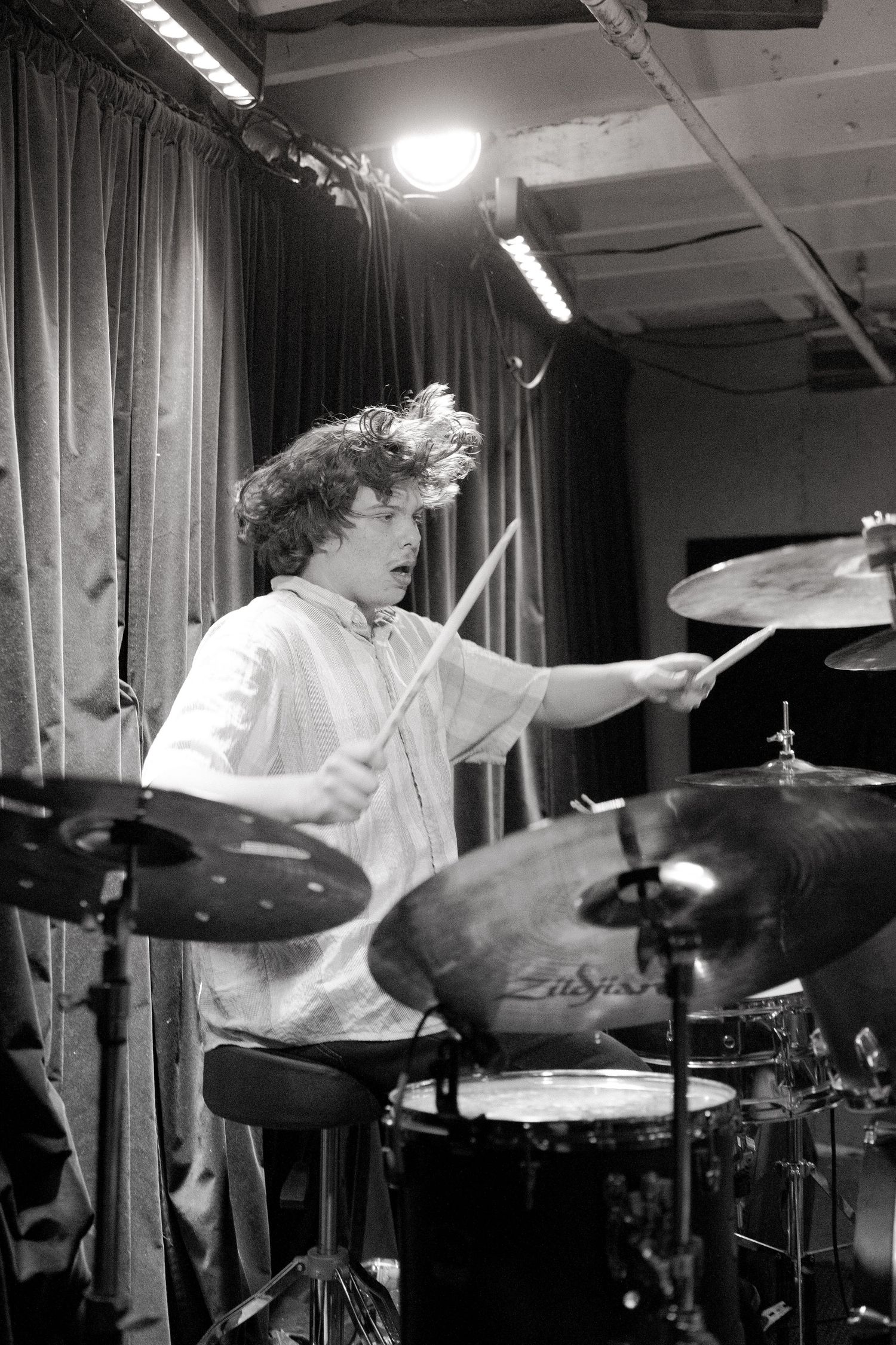 Series of black and white photos showing a drummer performing energetically with cymbals and drums on stage.
