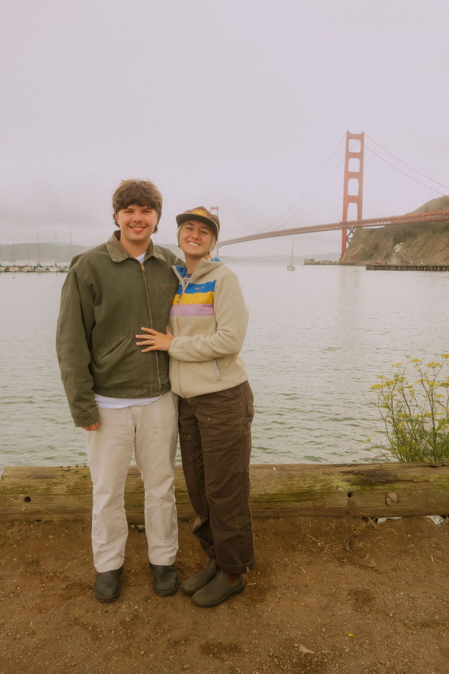 Two people embrace while standing on a path overlooking the iconic Golden Gate Bridge in San Francisco Bay.