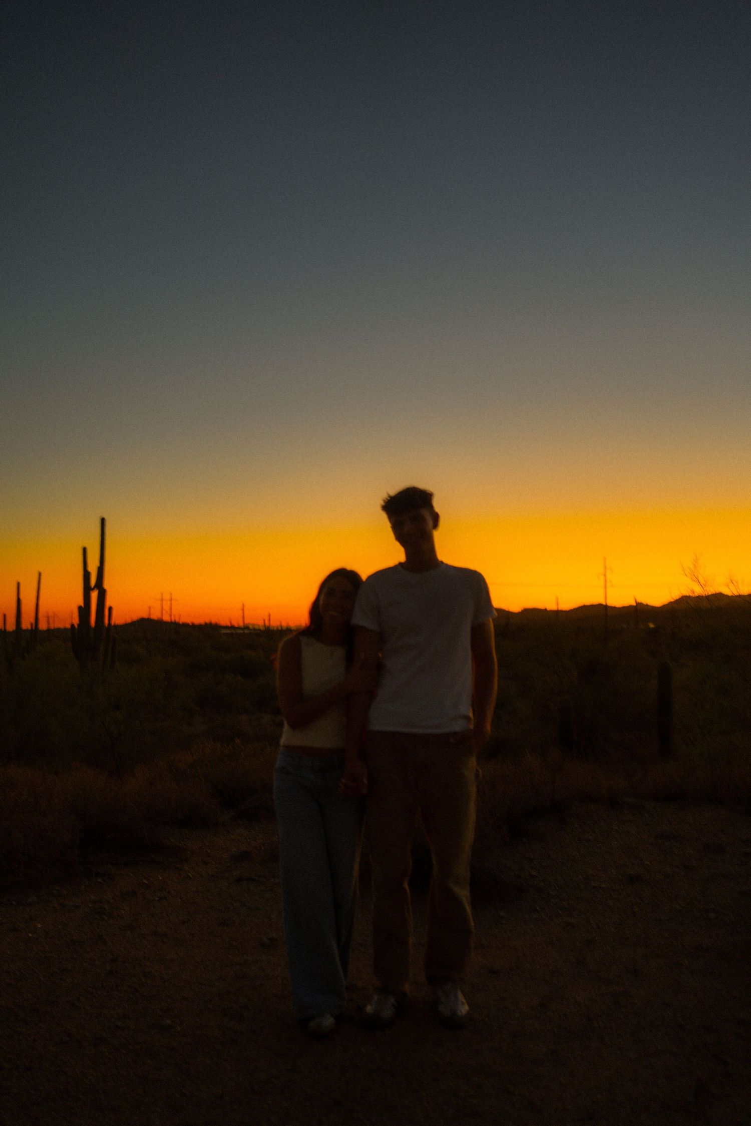 Silhouettes of people watching a vibrant orange sunset over desert landscape with saguaro cacti in the background.