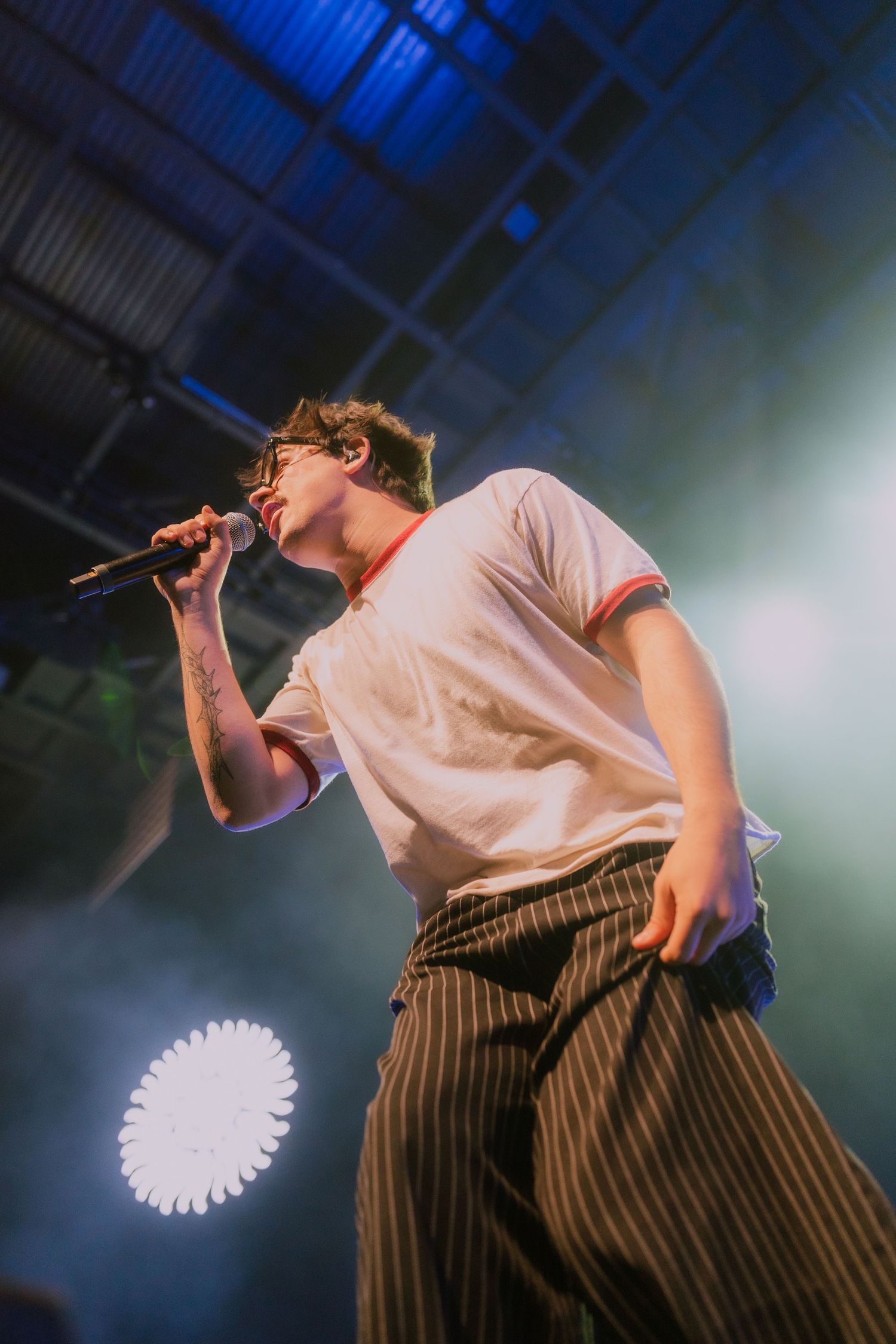 A performer in striped pants and white shirt sings on stage with dramatic lighting and fog effects in the background.
