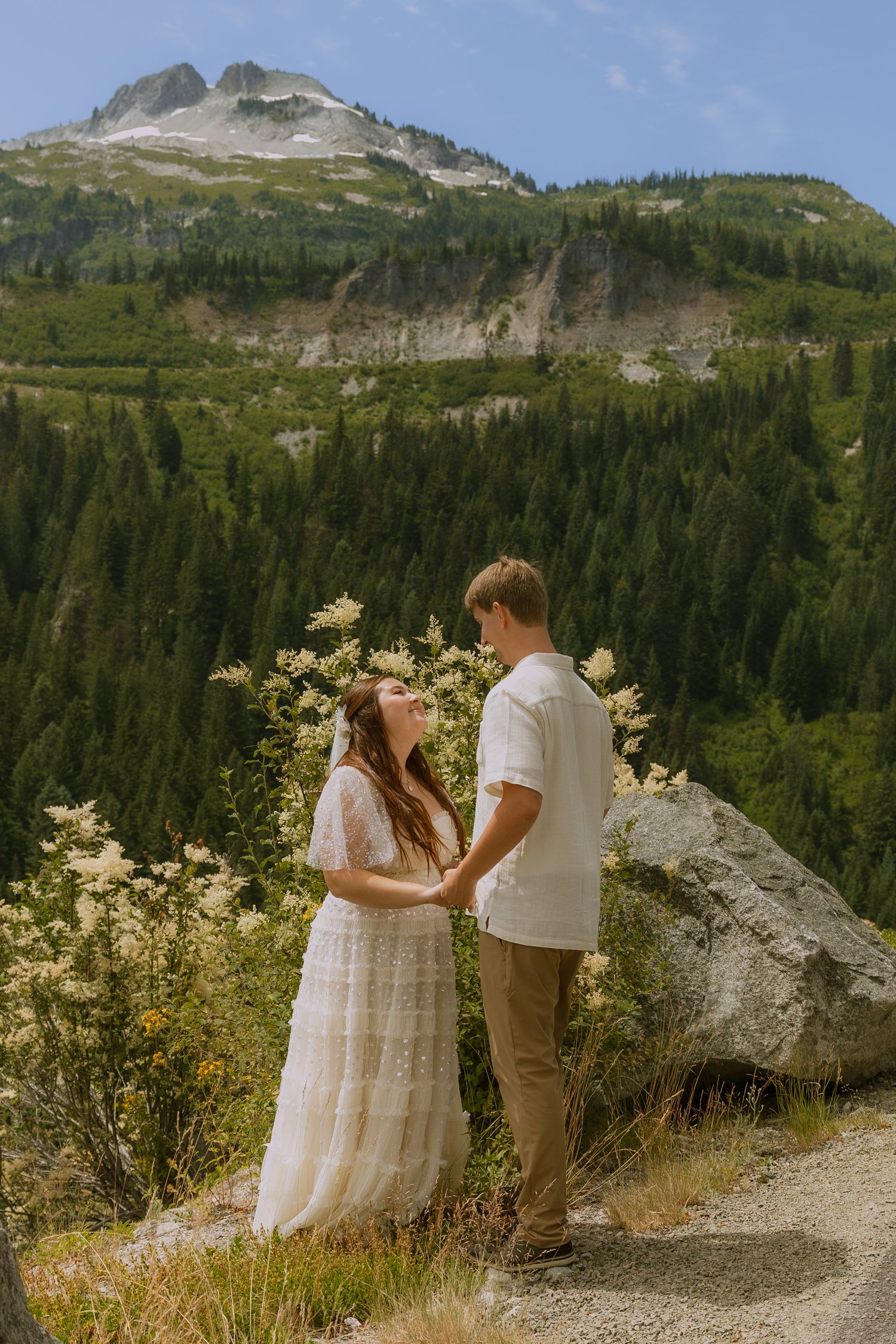 A couple shares an intimate moment against a backdrop of rugged mountain peaks and evergreen forests.