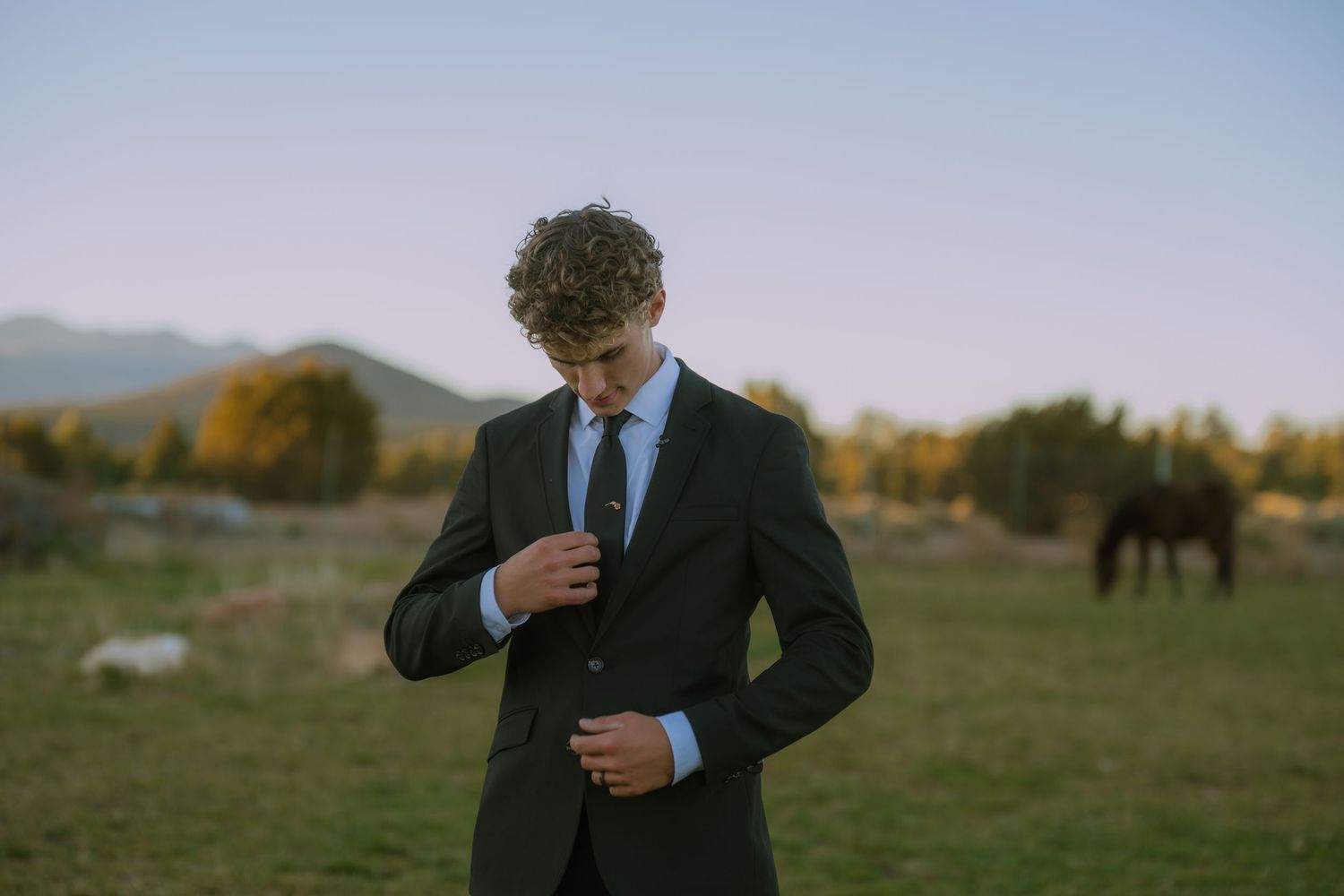 An elegant black suit and tie against a scenic mountain backdrop at sunset.