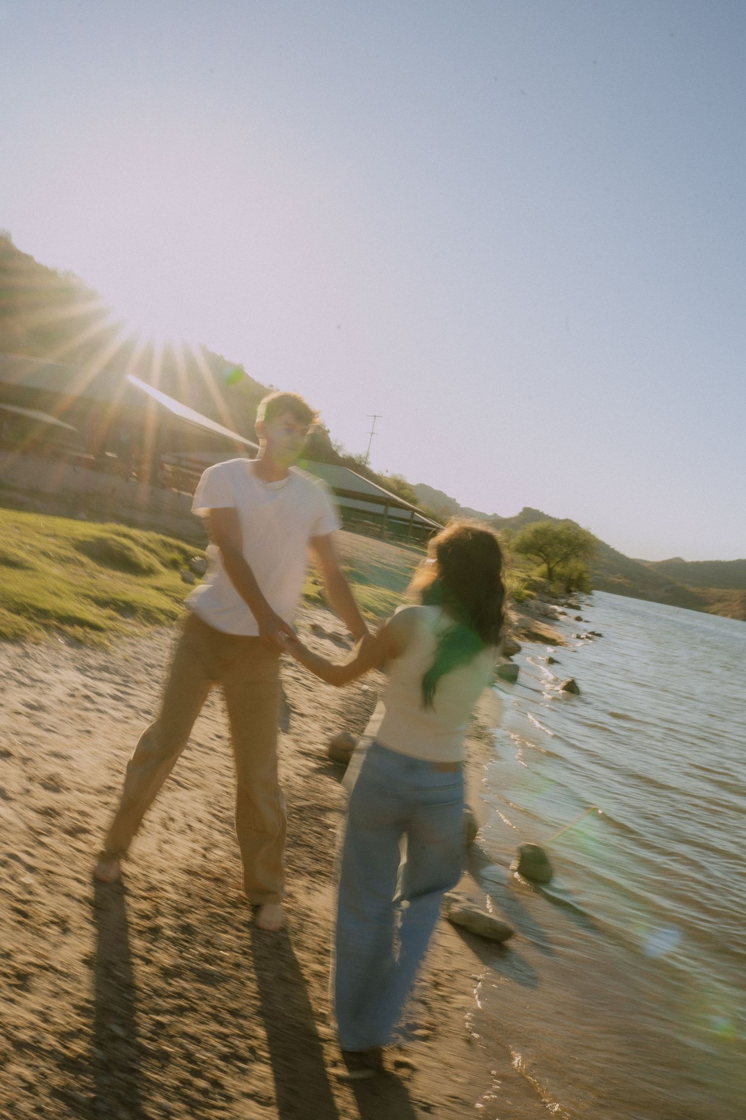 People enjoying a sunny day at the beach with lens flare and water reflections creating a dreamy summer atmosphere.
