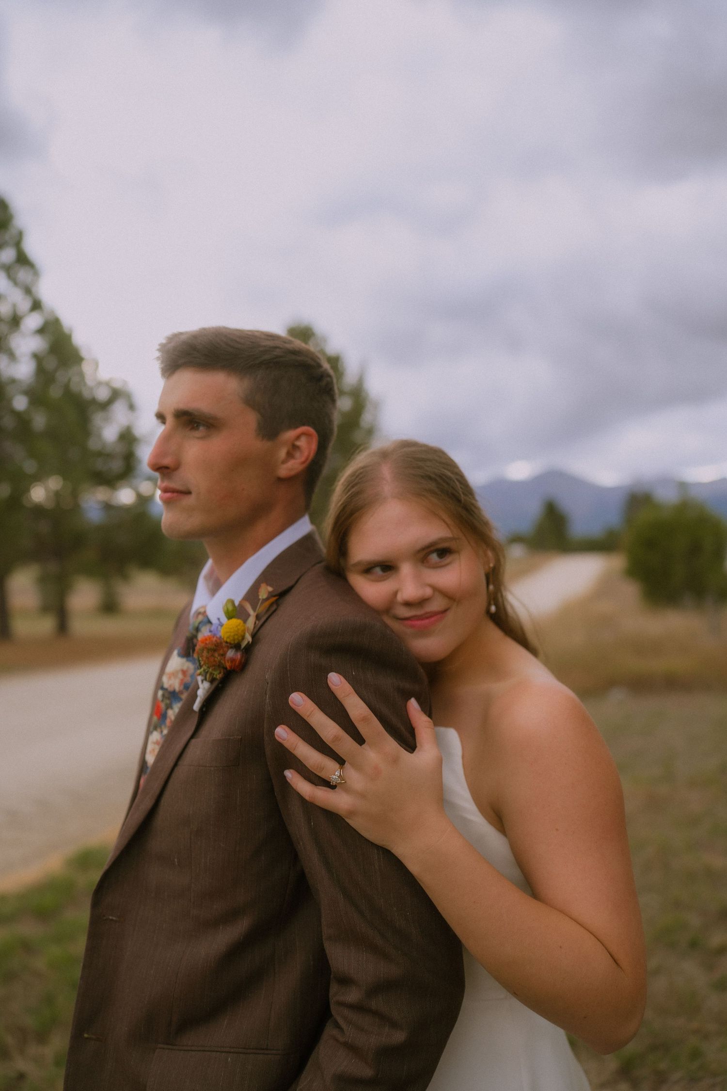 A couple shares an intimate moment outdoors against a cloudy mountain landscape.