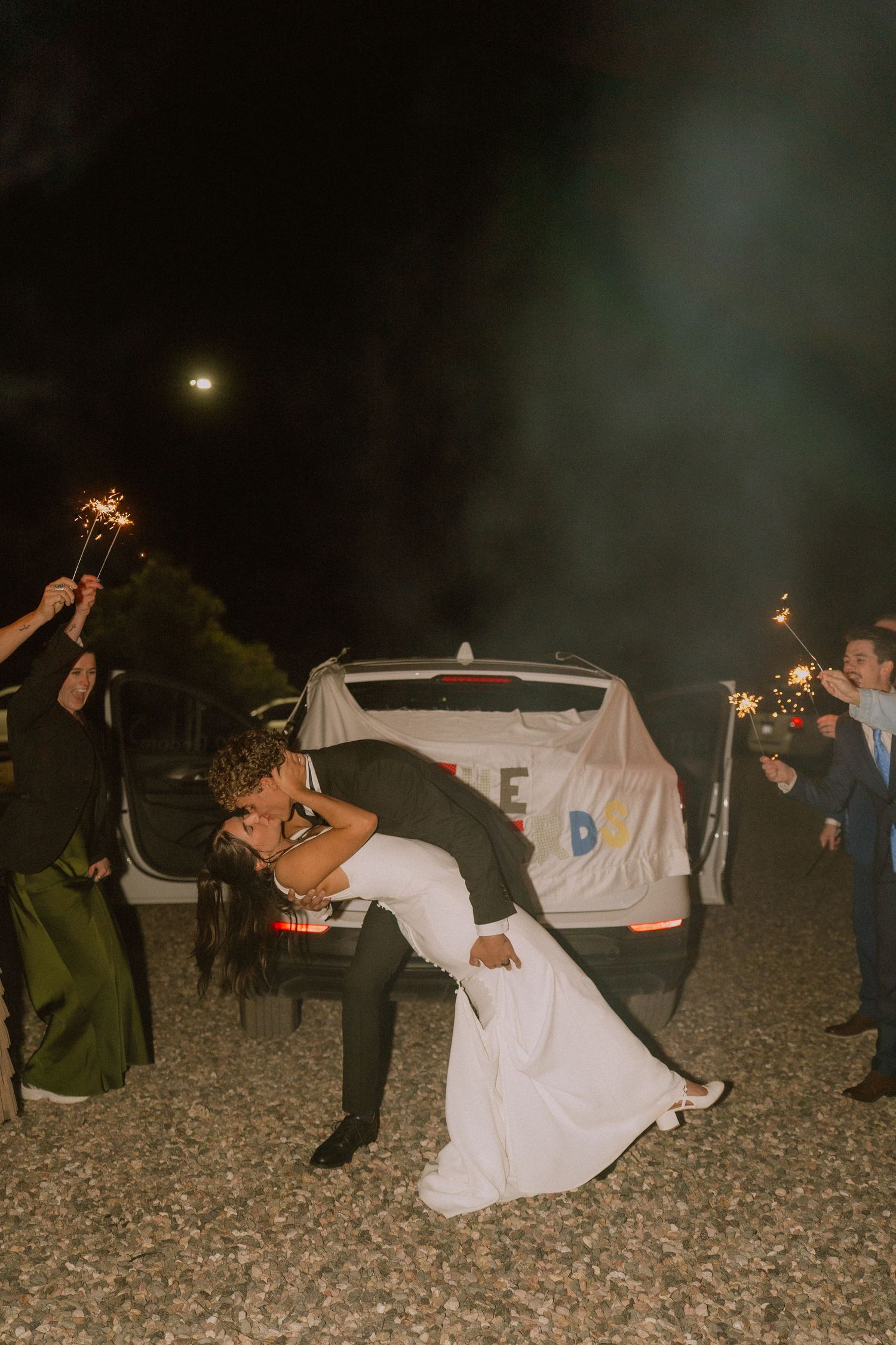 Wedding guests hold sparklers creating a magical nighttime send-off for the newlyweds.