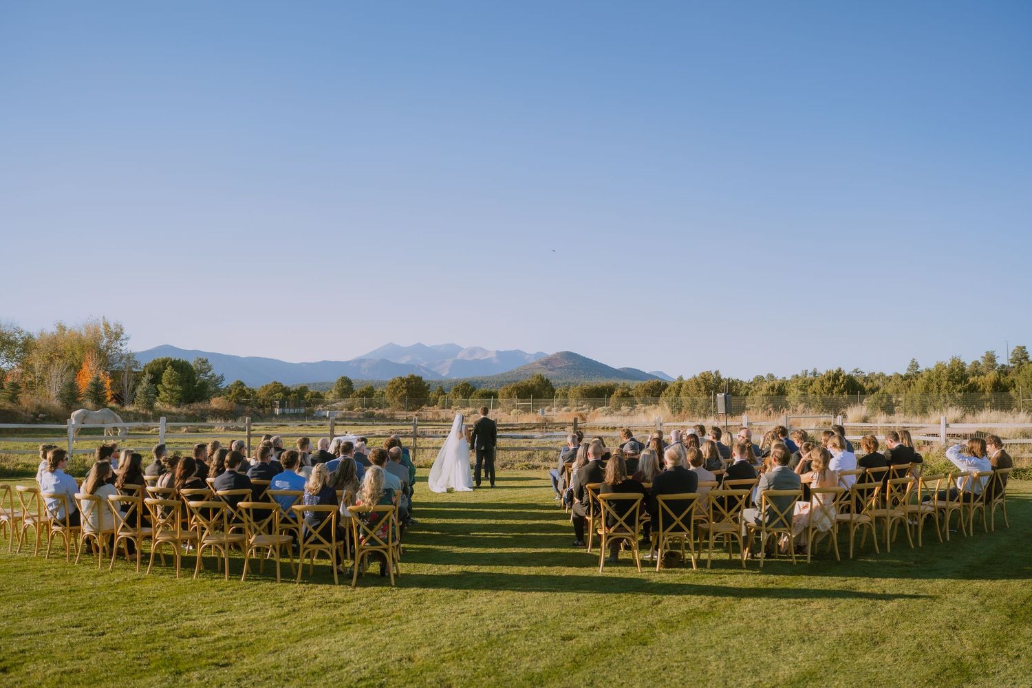 Panoramic view of an outdoor wedding ceremony with wooden chairs arranged in rows against a scenic mountain backdrop.