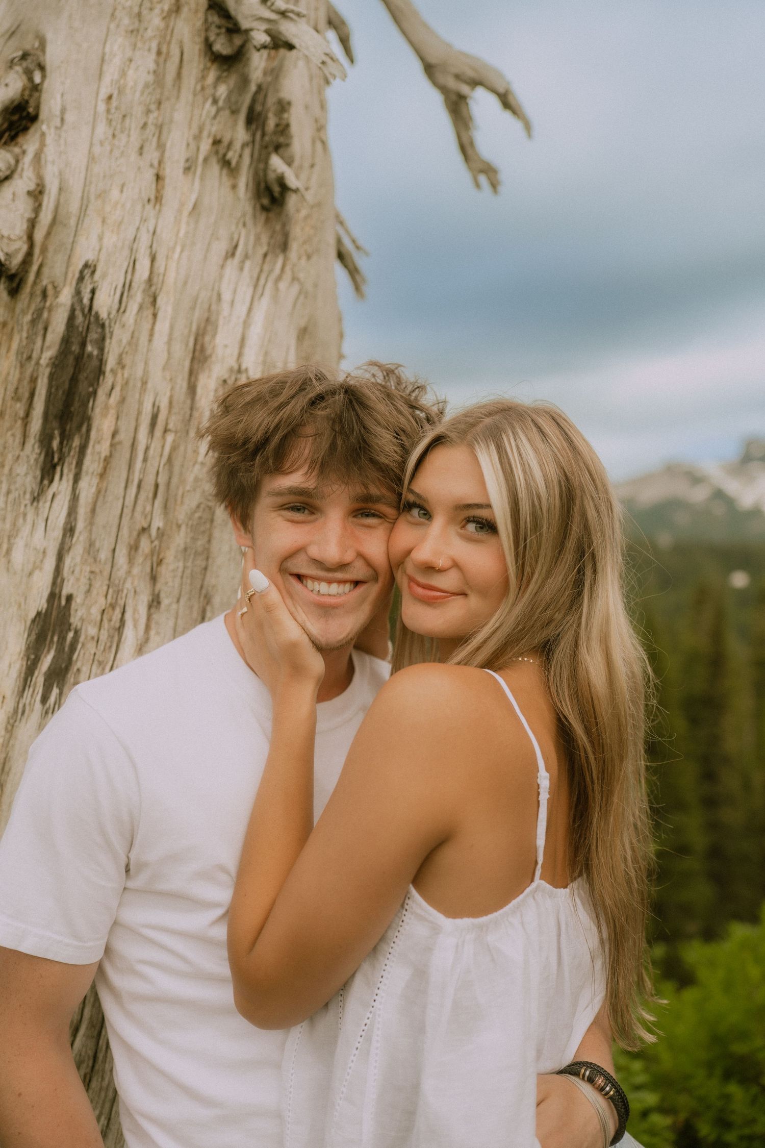 A romantic couple in white clothing share tender moments against a rustic tree backdrop in a series of candid photos.