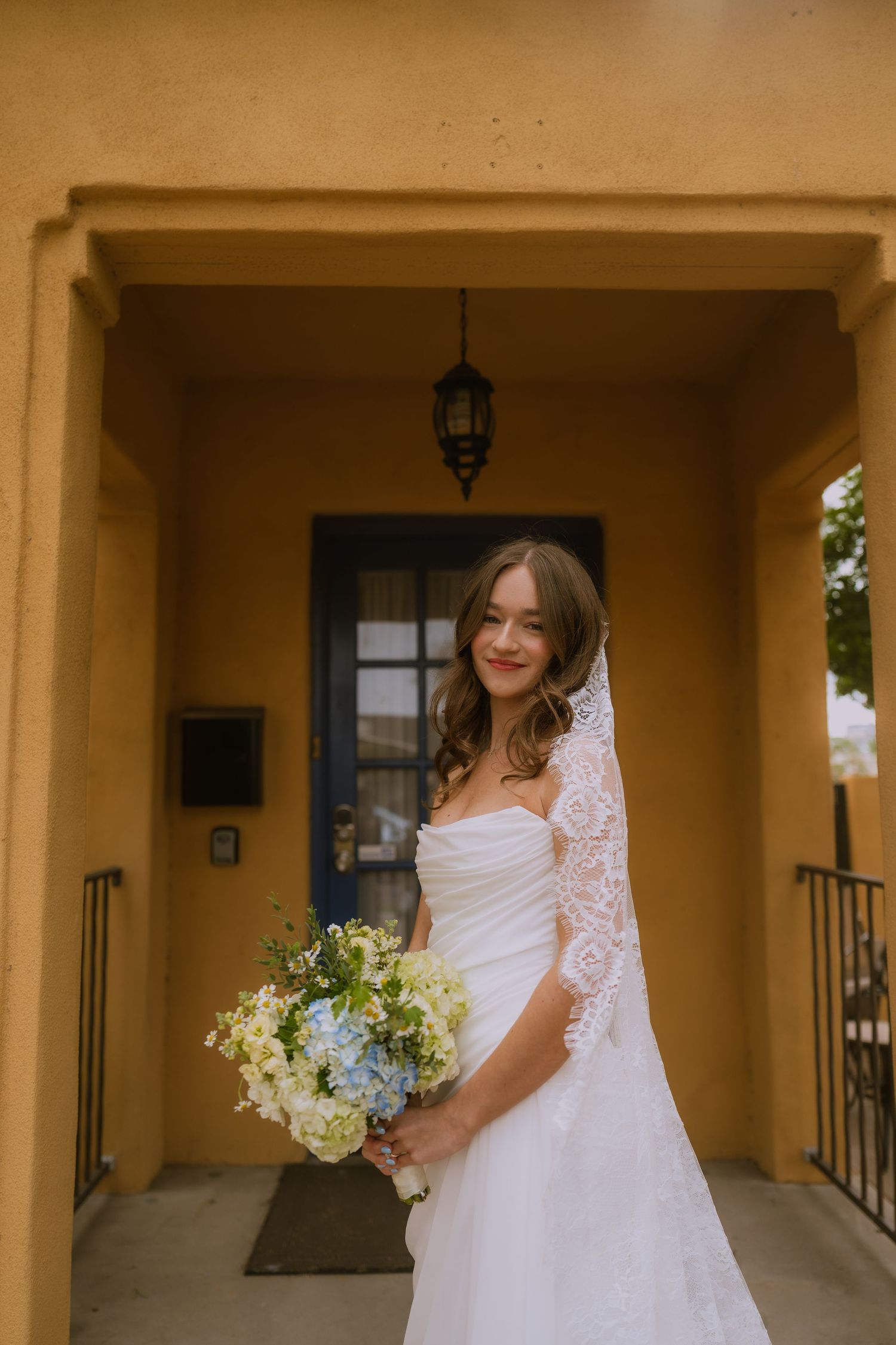 A bride in a white wedding dress holds a bouquet of white flowers while standing in an archway.