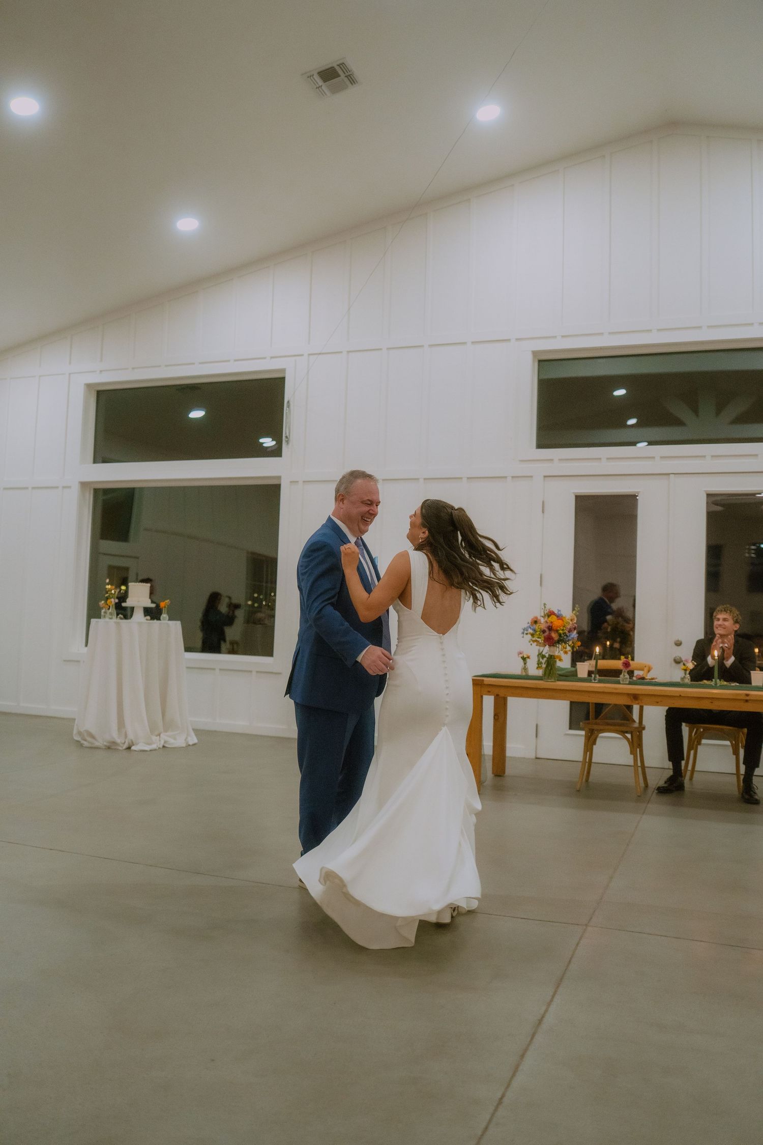 A couple dances together in a white indoor venue space with recessed lighting.