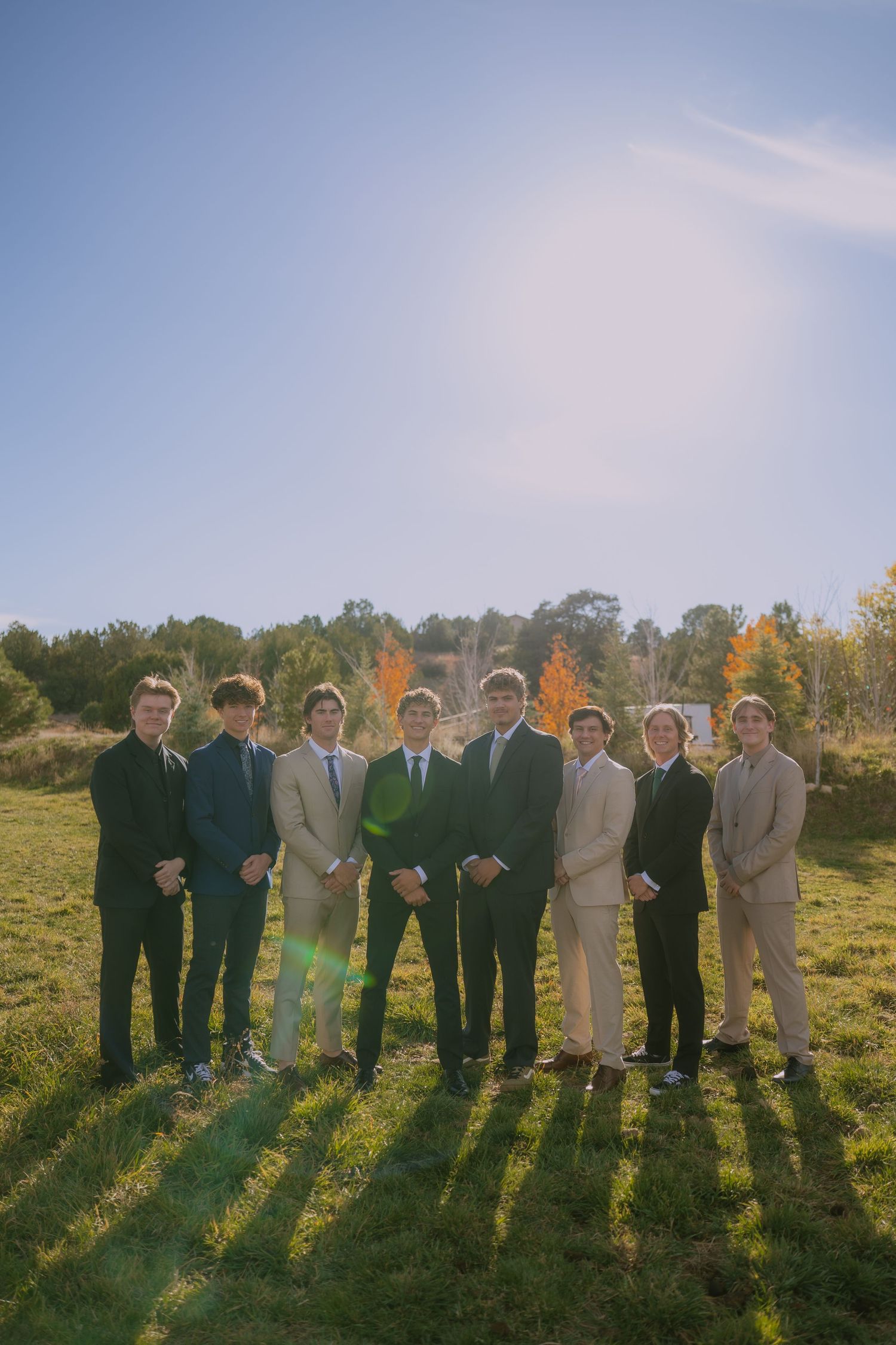 Wedding party members in suits standing in a row against a scenic fall landscape.