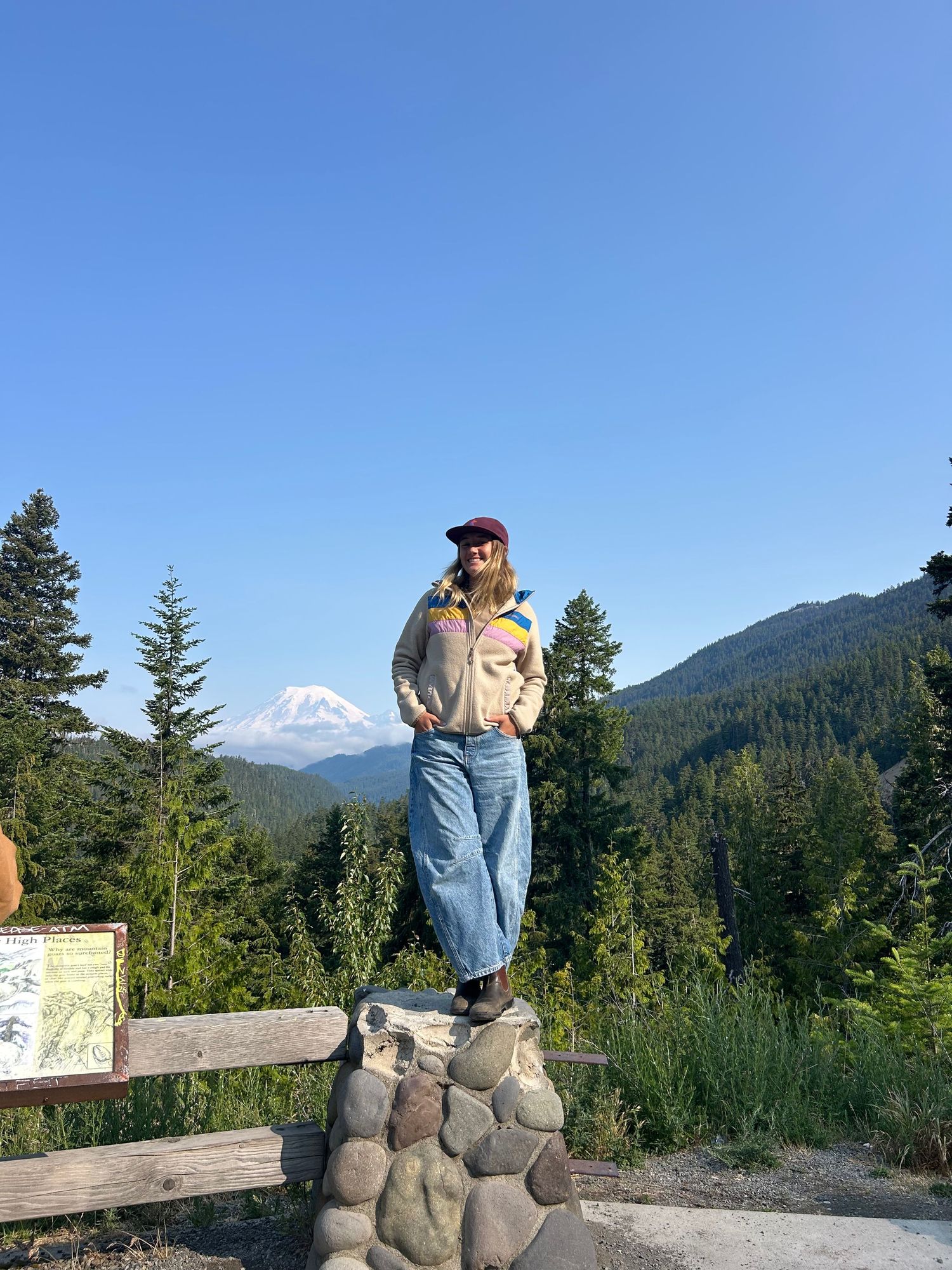 Someone stands on a stone pedestal with Mount Hood visible in the background on a clear summer day in Oregon.