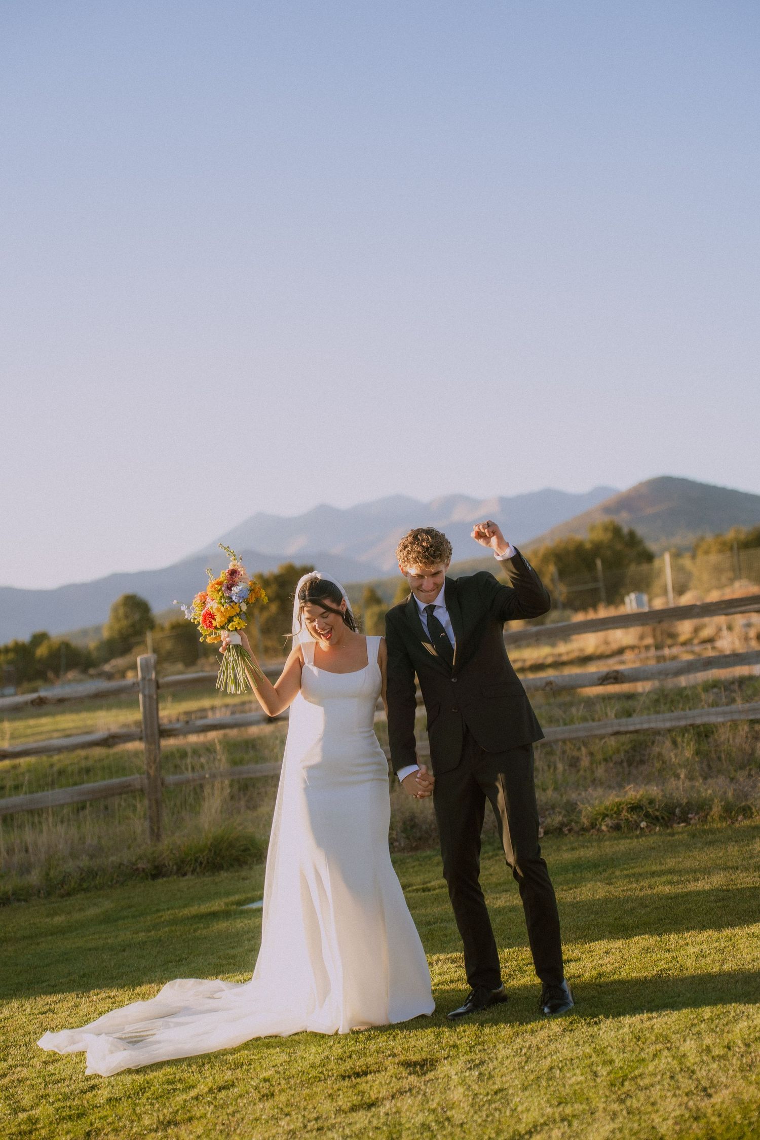 A wedding couple poses in a field with mountain views during their outdoor ceremony.