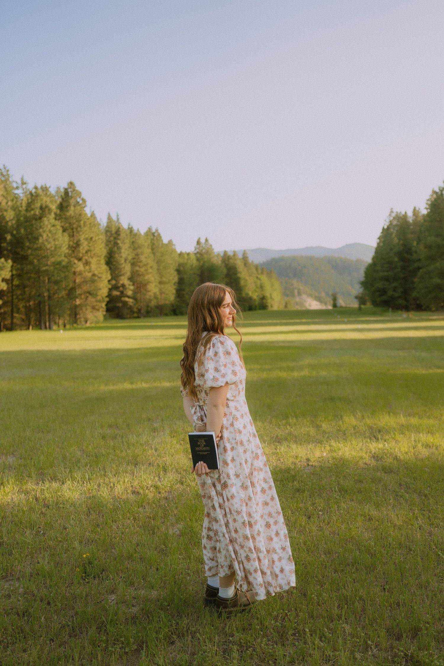 A flowing floral dress stands out against a green meadow and mountain landscape at golden hour.