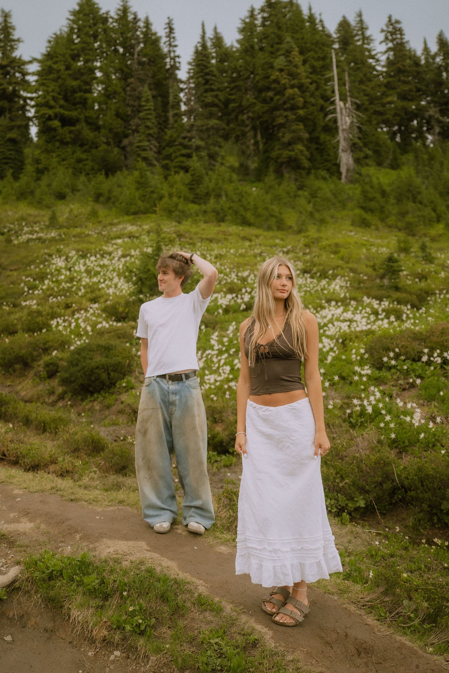 People dancing and twirling on a mountain trail surrounded by evergreen trees and wildflowers.
