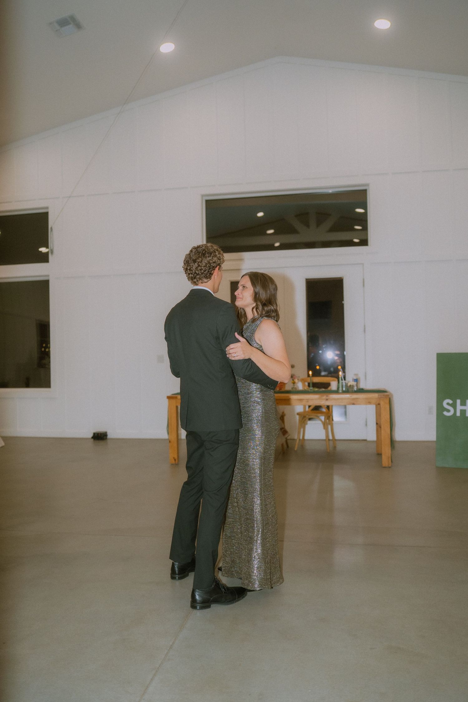 Couples dance together in an elegant white-walled reception venue with wooden furniture.