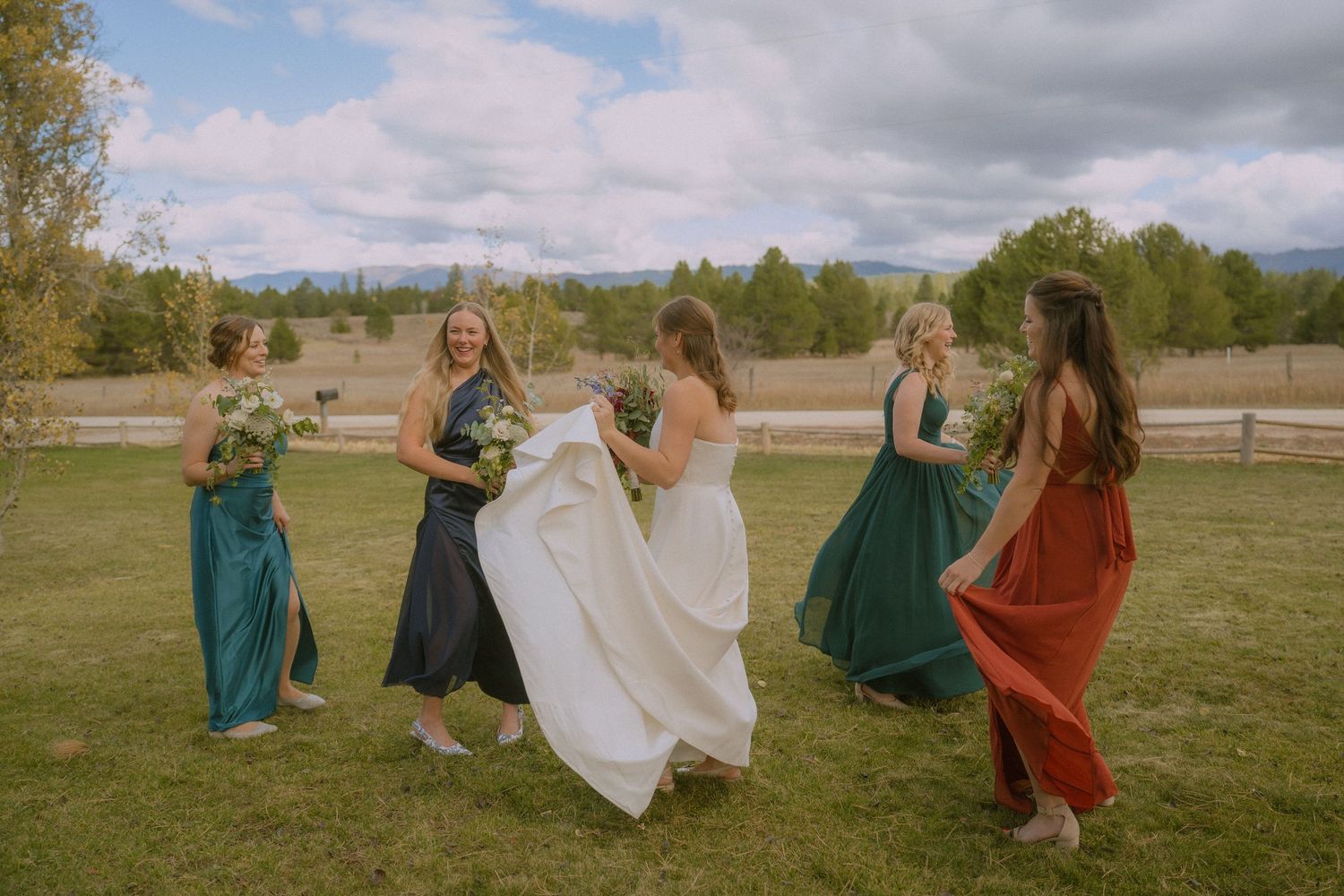 A group in formal attire dances together in a grassy field on a cloudy day.