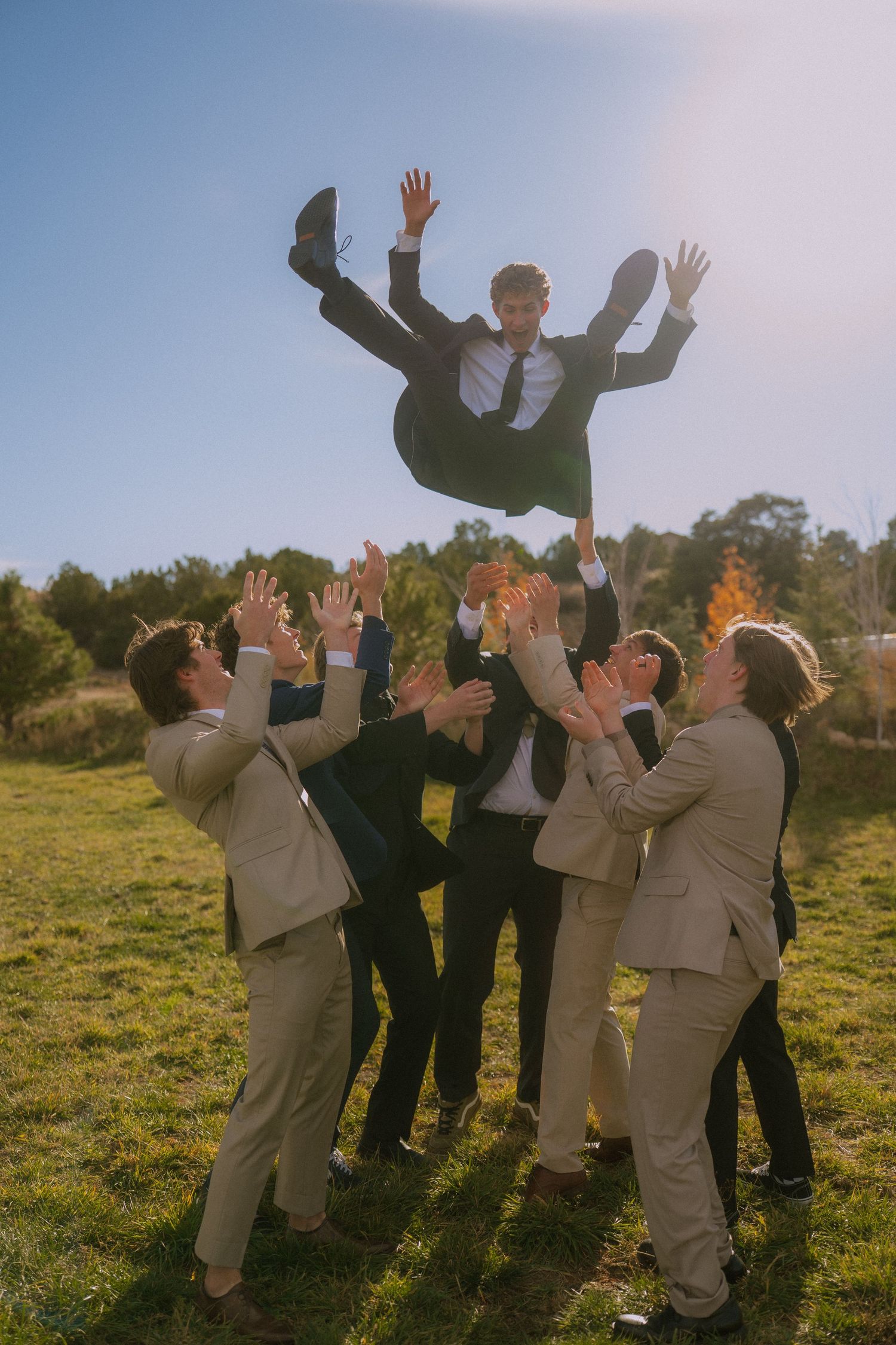 Wedding party members playfully jumping and posing together on a grassy hillside.