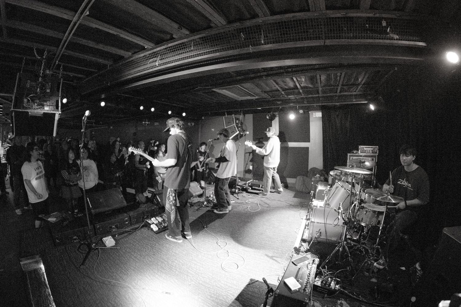 Black and white panoramic sequence showing a live band performing on stage in a dimly lit venue.