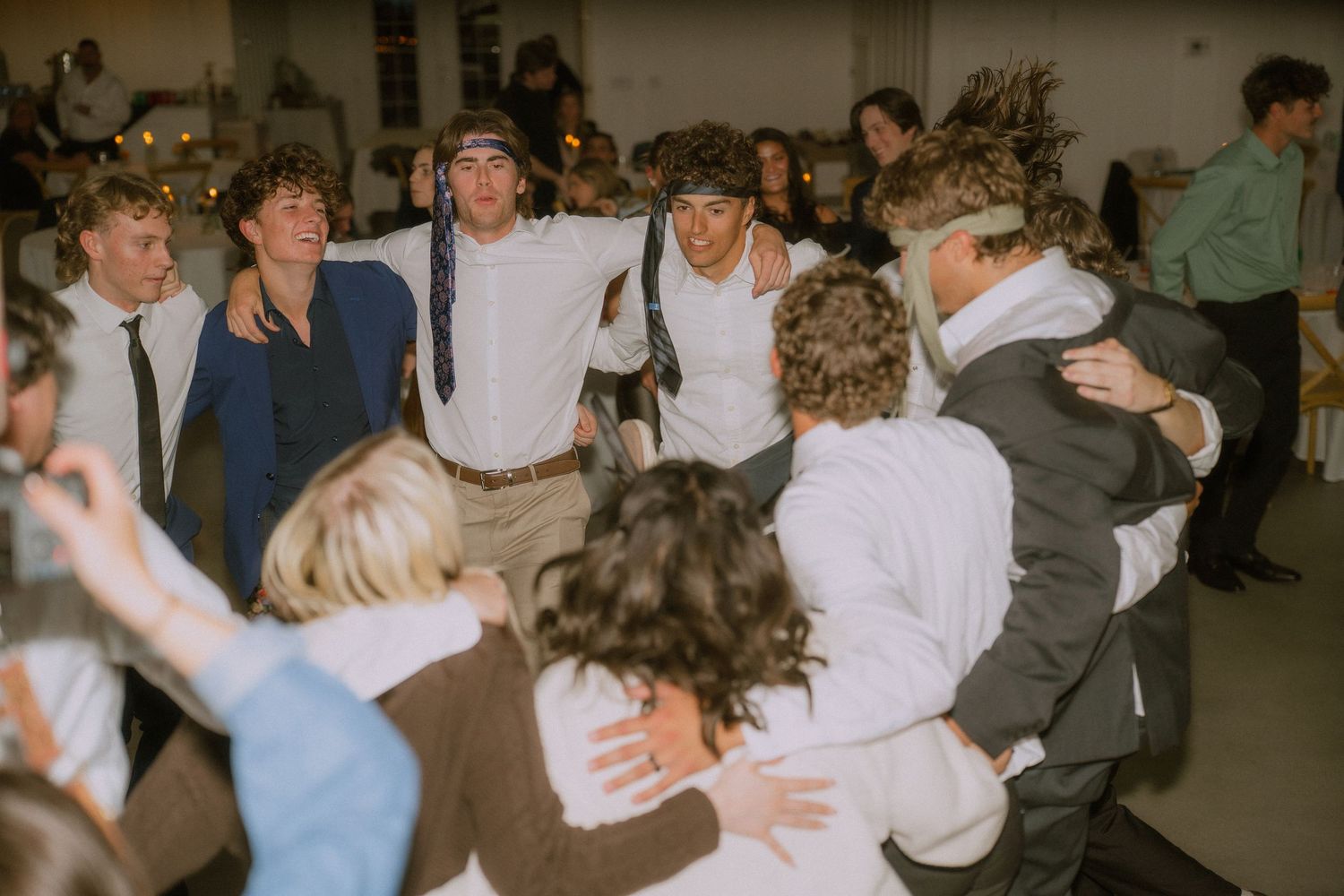 Wedding guests dance and celebrate at a lively indoor reception.