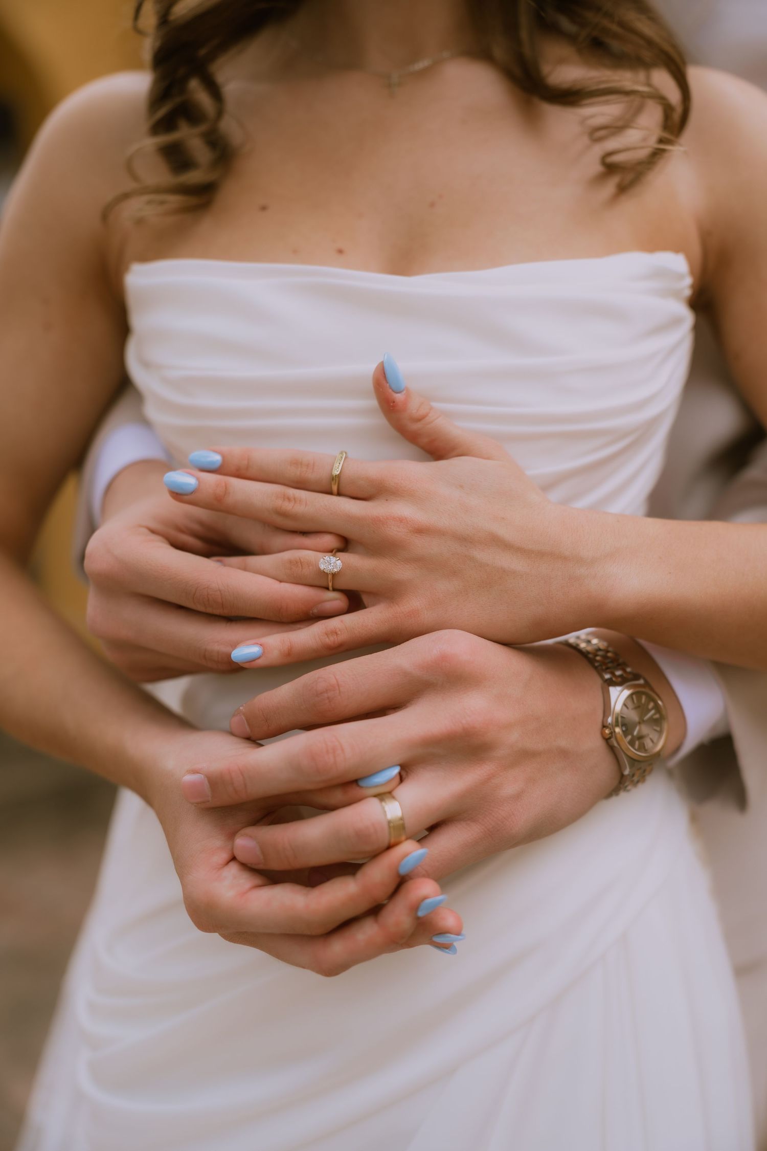 Close-up shots of hands with light blue nail polish and wedding rings against a white dress background.