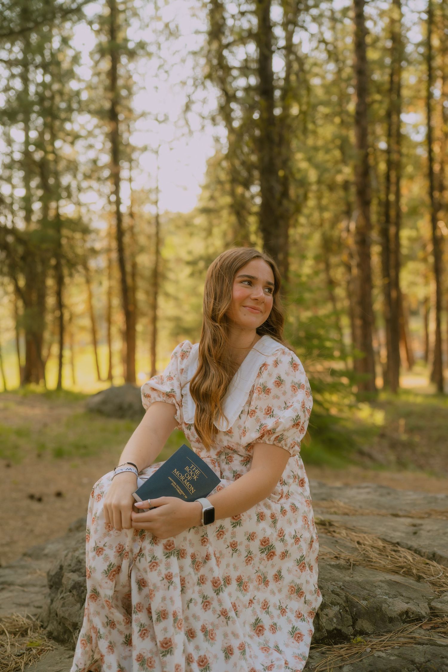 A white floral dress catches golden light while sitting peacefully in a serene forest scene.