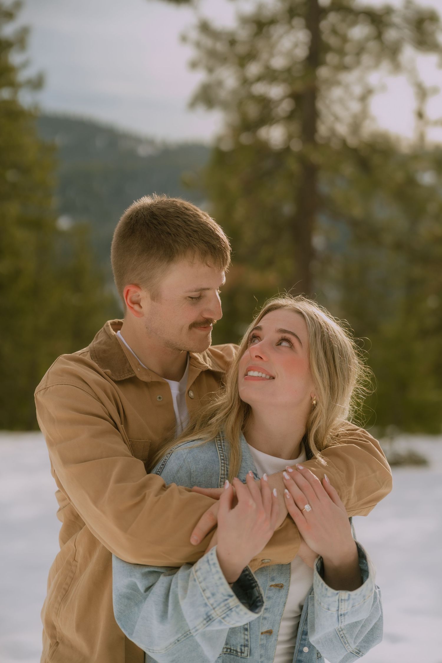 A couple shares playful and intimate moments in a snowy winter landscape while wearing casual outerwear.