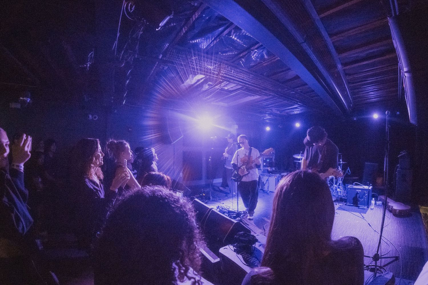 Concert performers on stage illuminated by vibrant blue lighting during a live music performance at a venue.