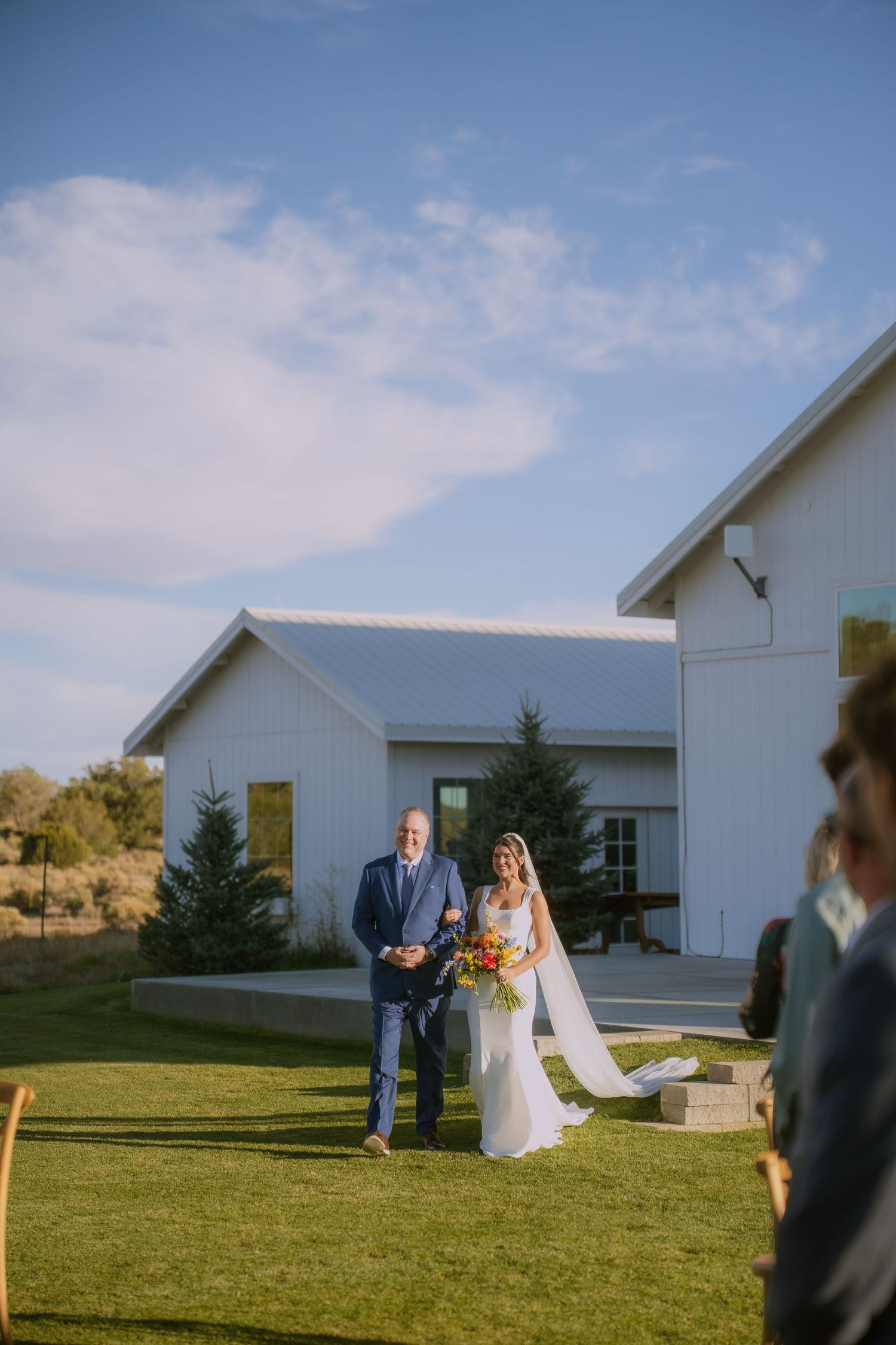 White wedding venue building sits on a grassy lawn under blue skies.