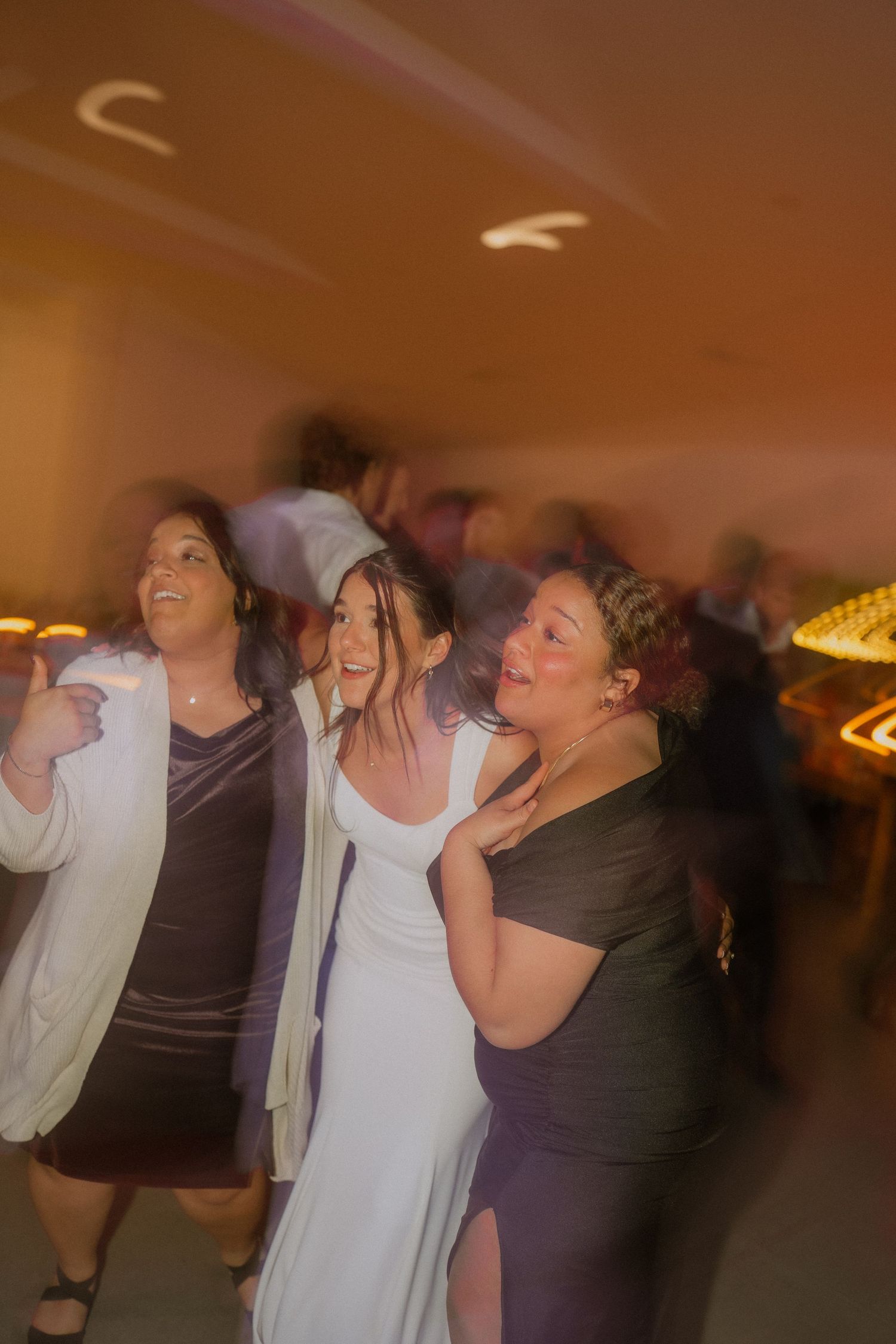 Wedding reception dance party with guests enjoying themselves in dimly lit indoor venue.