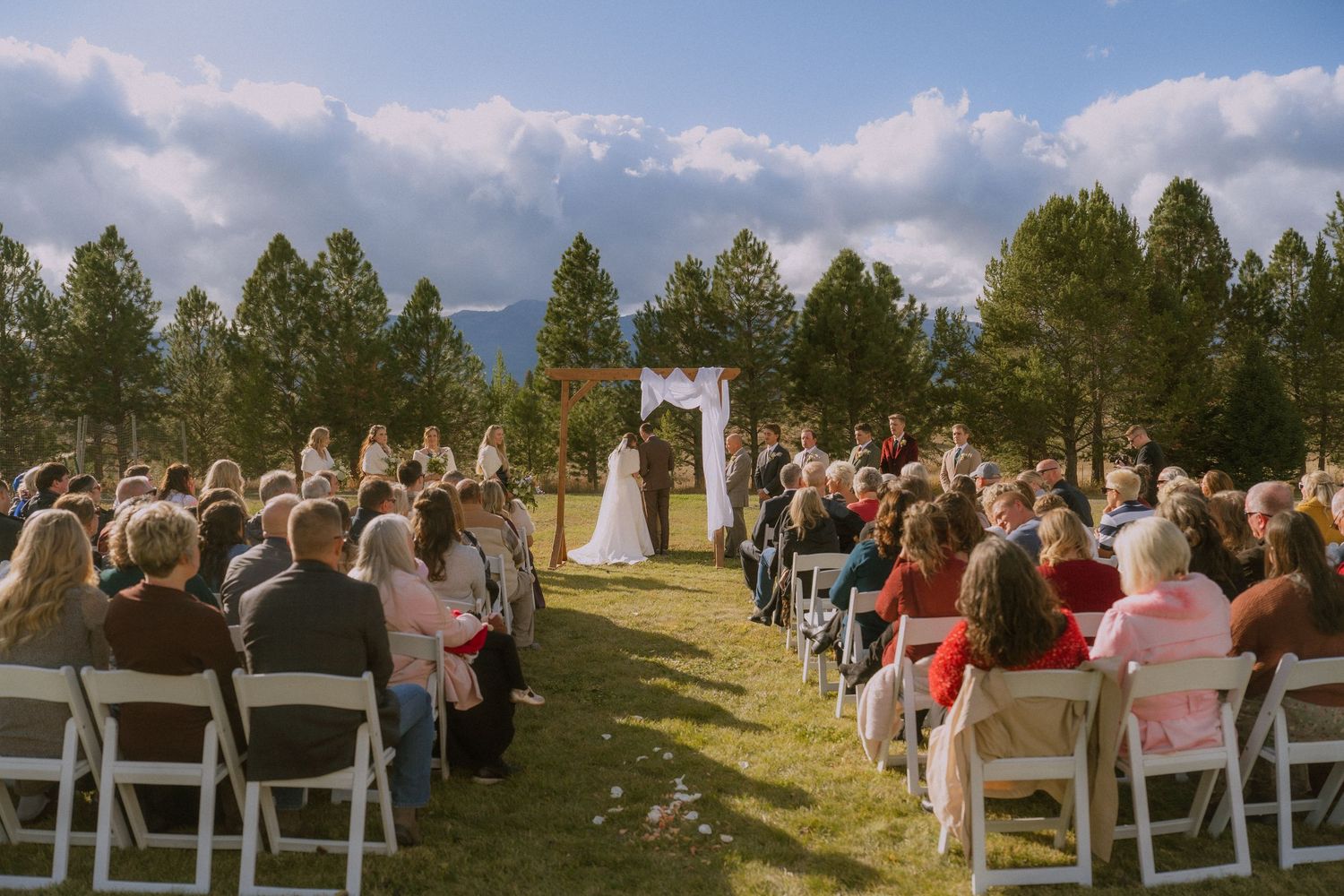Panoramic view of outdoor wedding ceremony setup with white chairs arranged in rows under a bright blue sky.