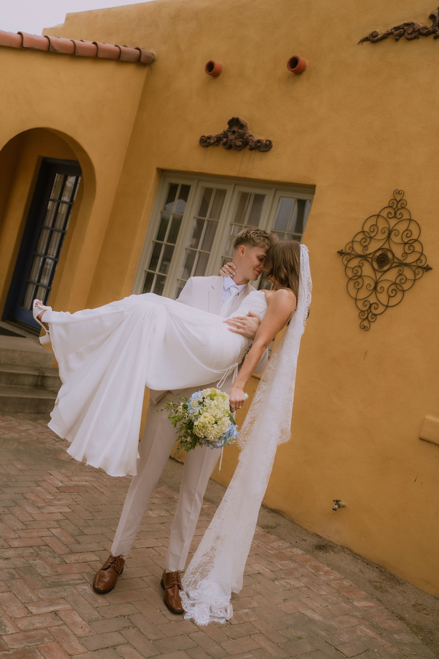 A series of romantic wedding photos showing a couple in white attire posing against a yellow stucco wall.