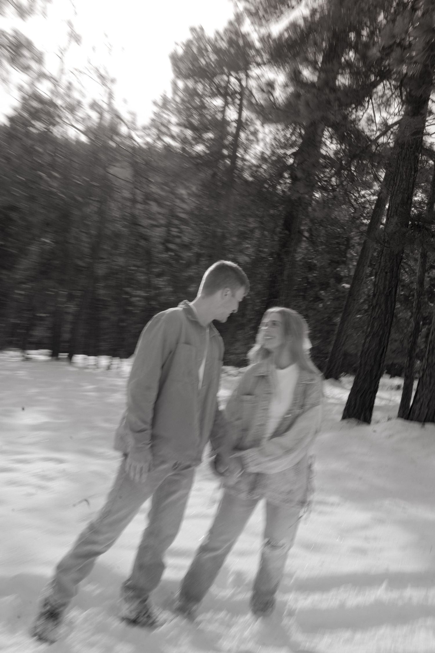 Motion blur captures two people walking through a snowy forest landscape in winter.