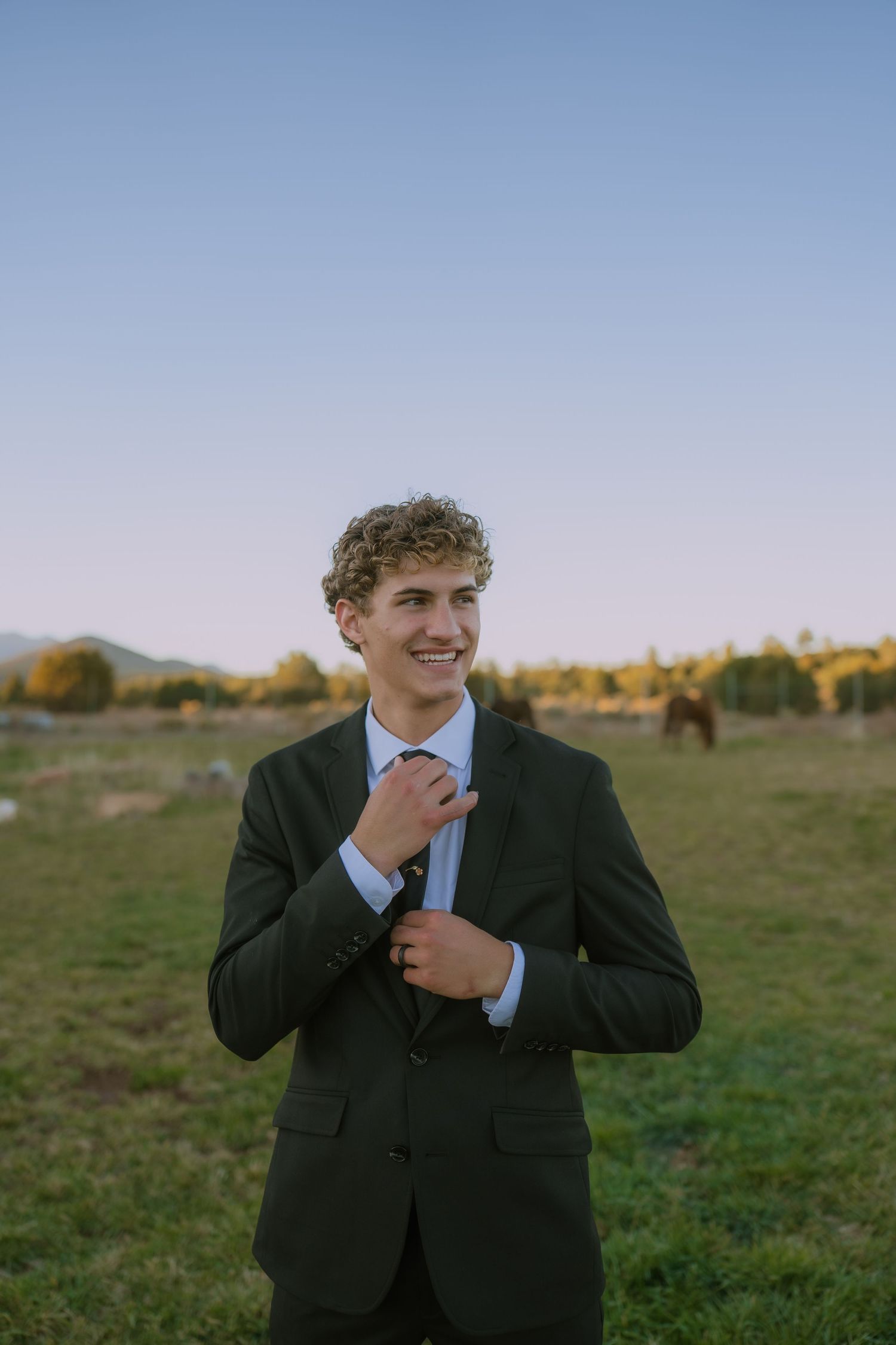 A person in a dark suit stands in an outdoor field during golden hour, showing joyful body language.