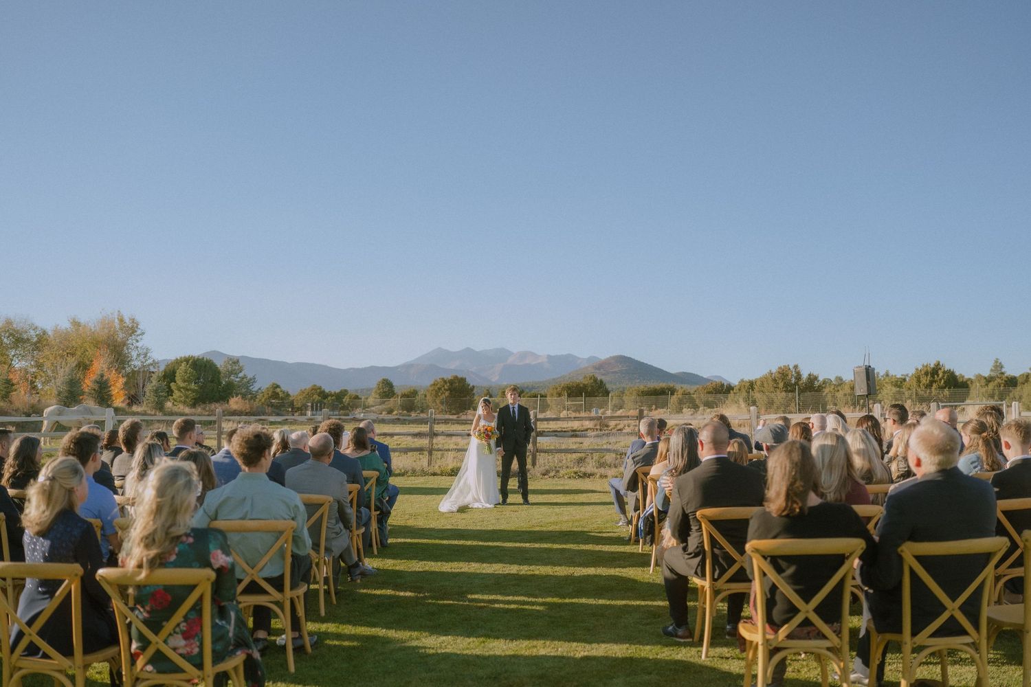Outdoor mountain wedding ceremony setup with wooden cross-back chairs and stunning mountain vista backdrop.