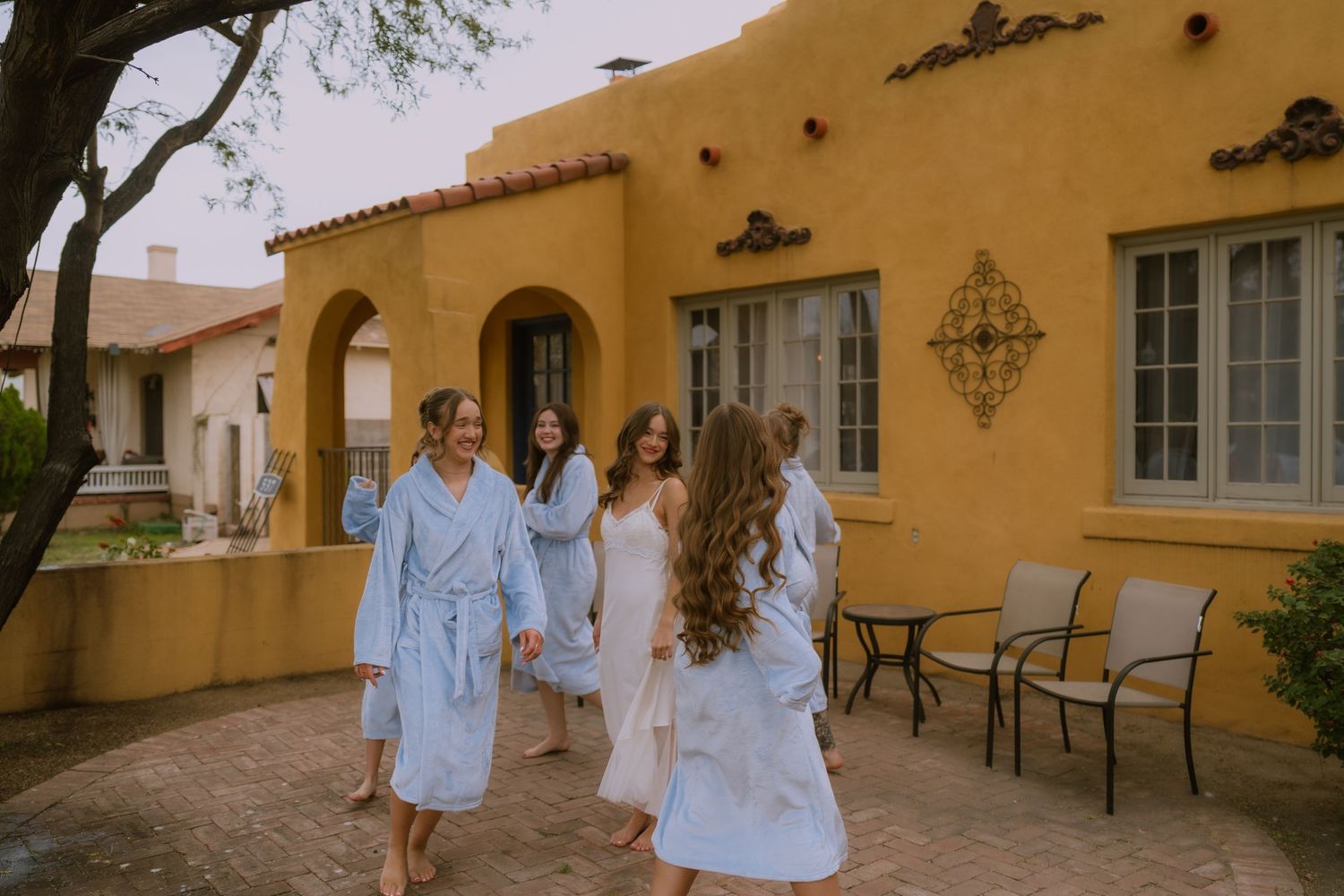 A group walks together along a Mediterranean-style building exterior with yellow stucco walls and arched windows.