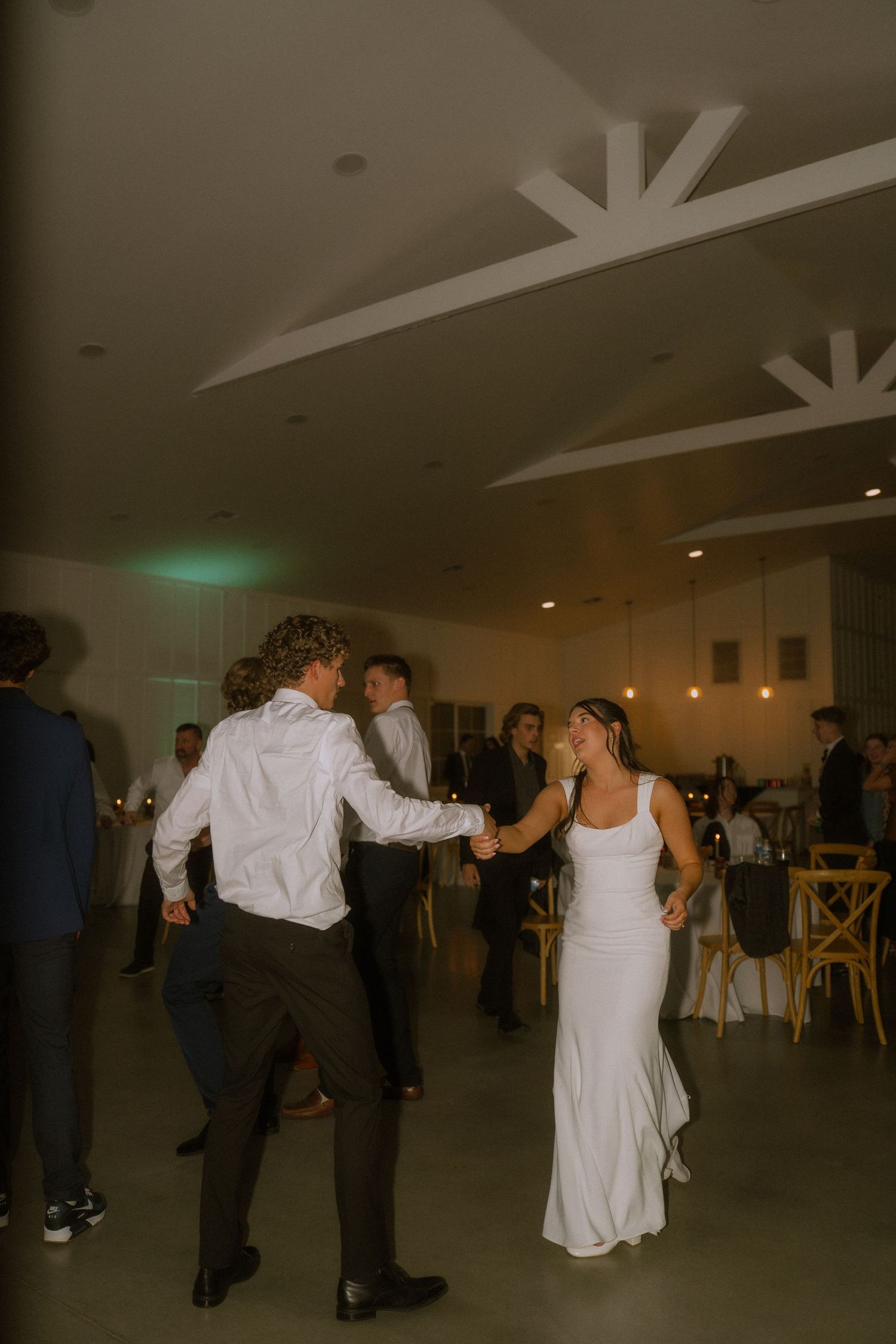 Wedding guests dancing in a spacious reception hall with geometric ceiling details.