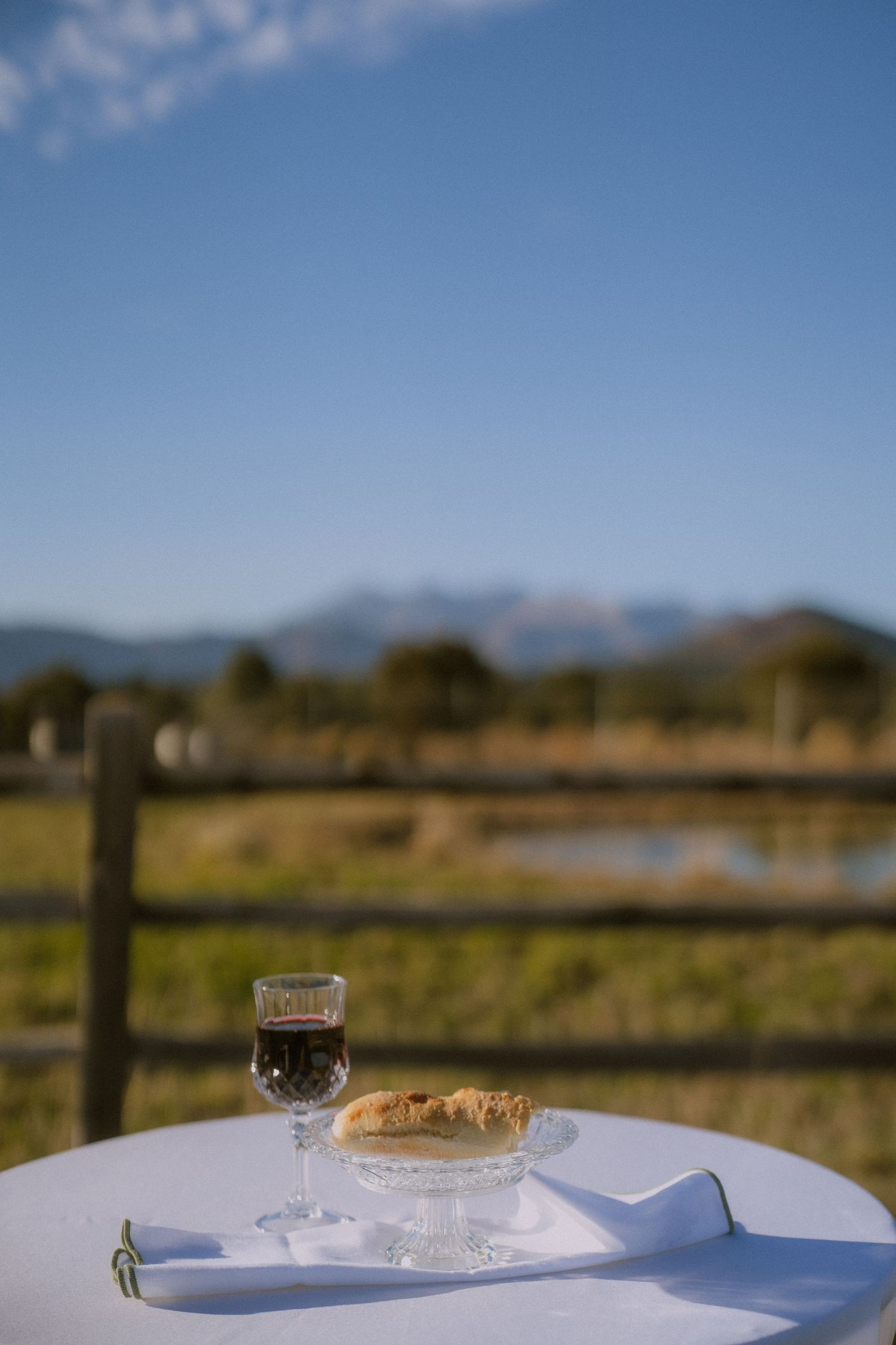 Wine glass and pastry on white tablecloth with mountain landscape in background.