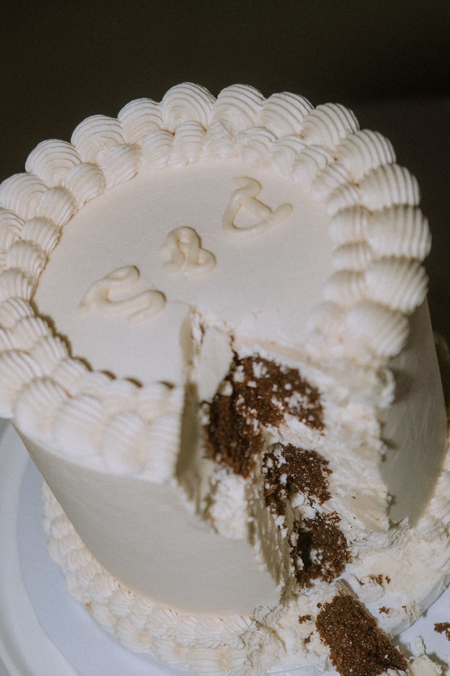 White wedding cake with decorative piping shows chocolate interior after being cut.