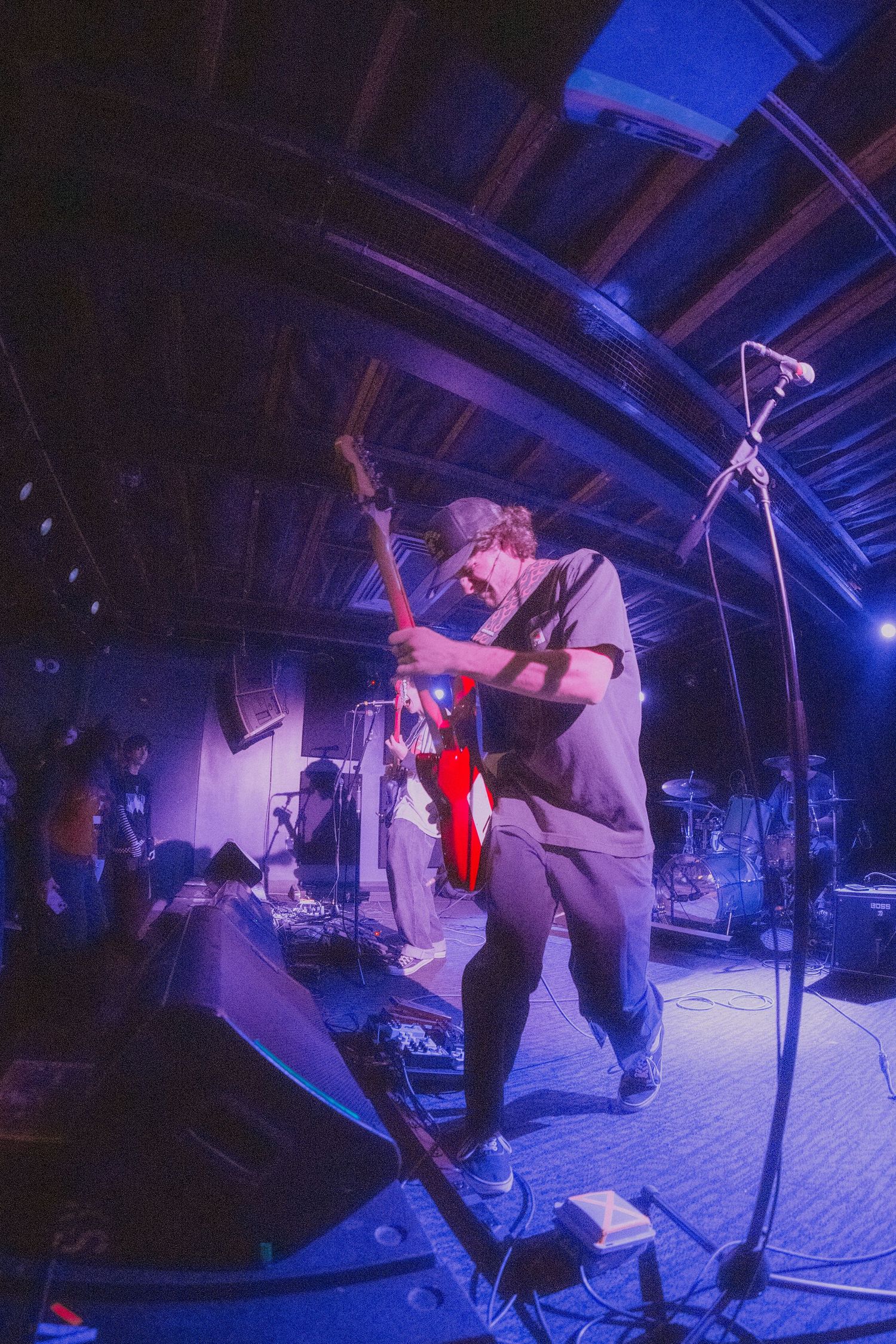 A musician performs on stage with a guitar under purple and blue lighting at an intimate concert venue.