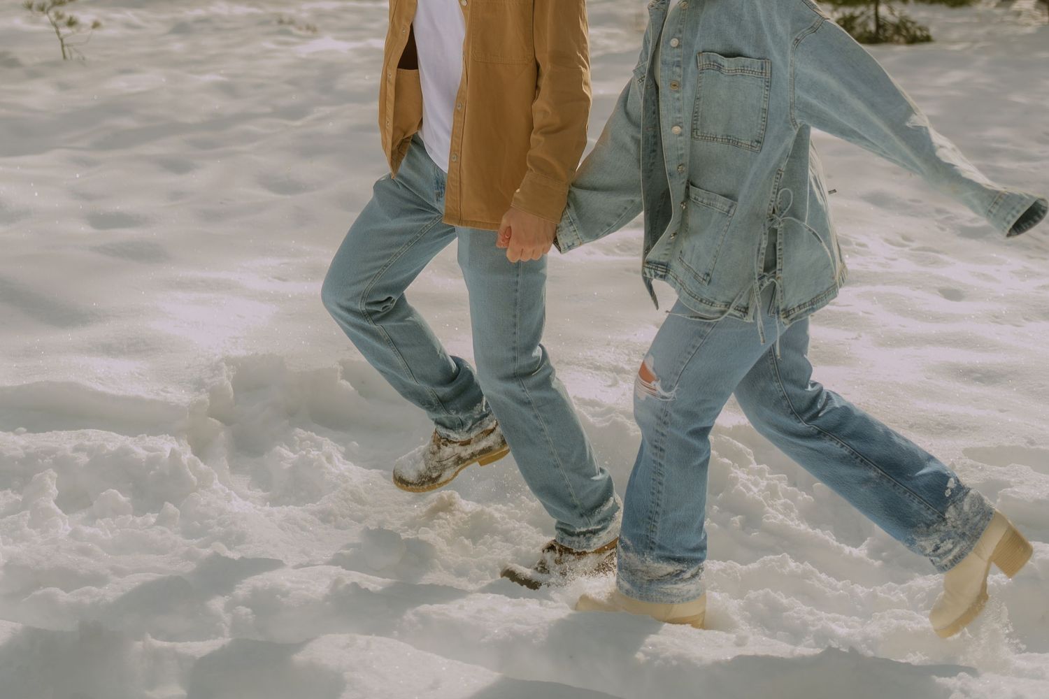 Multiple pairs of legs in jeans and brown shoes walking across a snowy surface in winter.